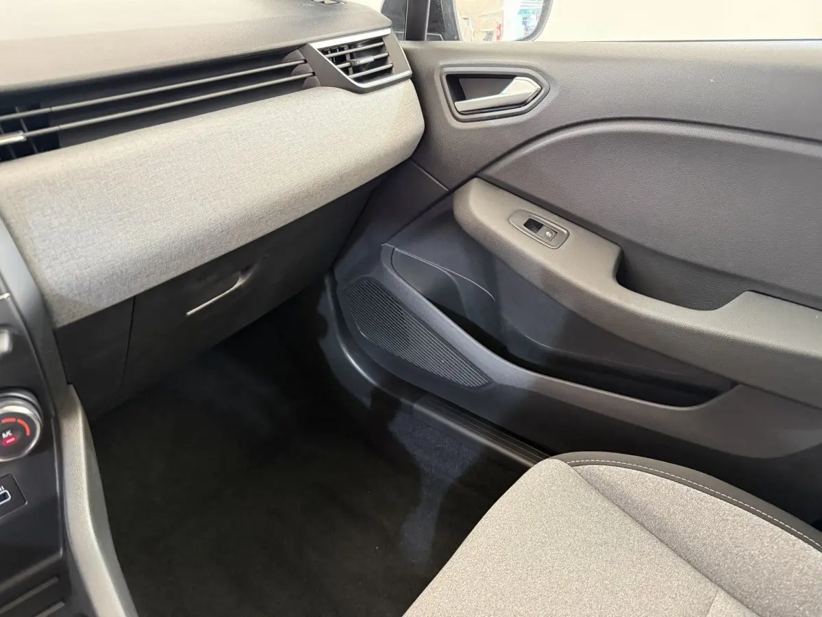 Intérieur de la Renault Clio 2025, vue côté passager avant, tableau de bord gris clair et porte noire.