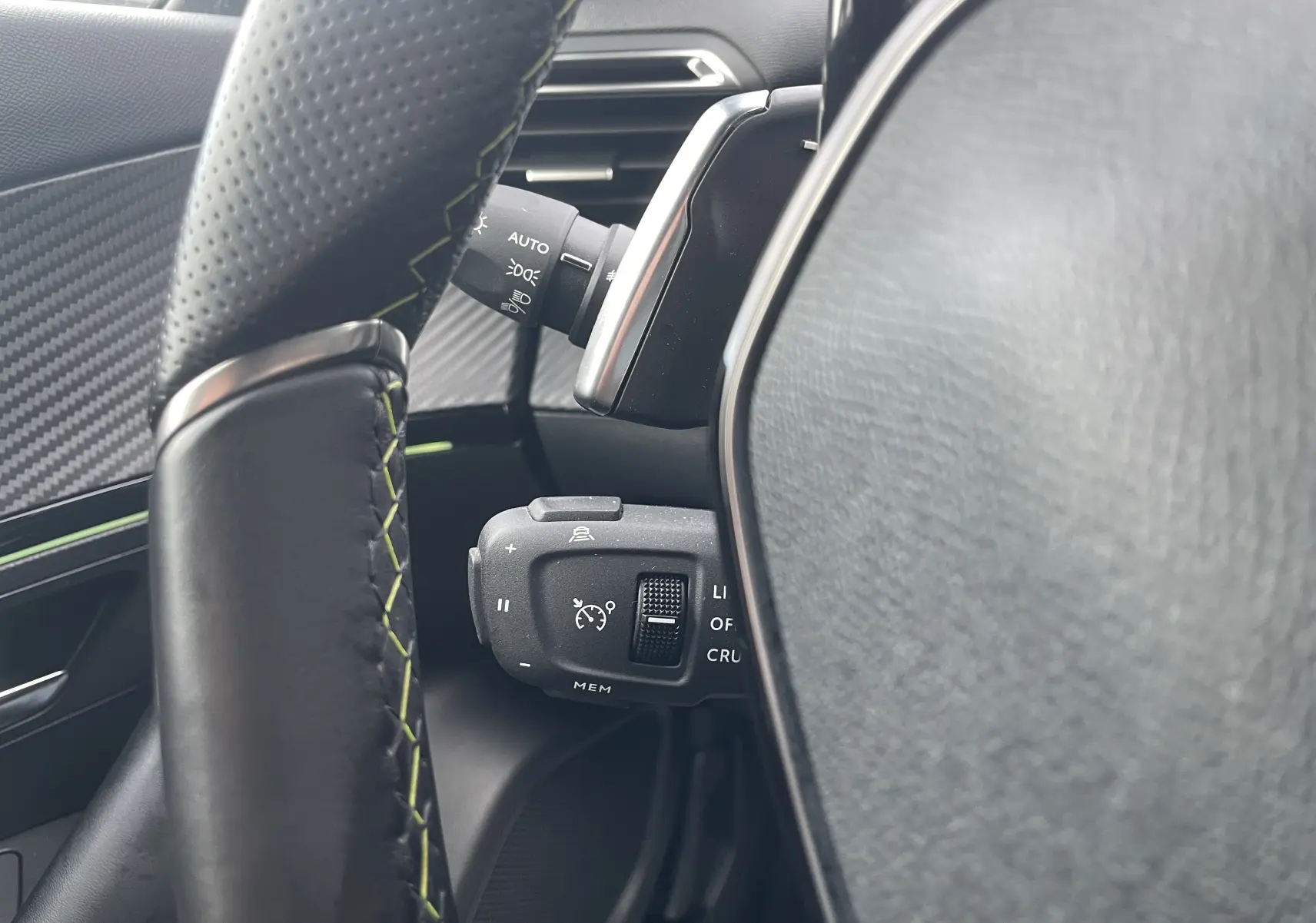 Gros plan sur le volant noir avec surpiqûres vertes et commandes de régulateur de vitesse d'une Peugeot 2008 gris Artense 2022.