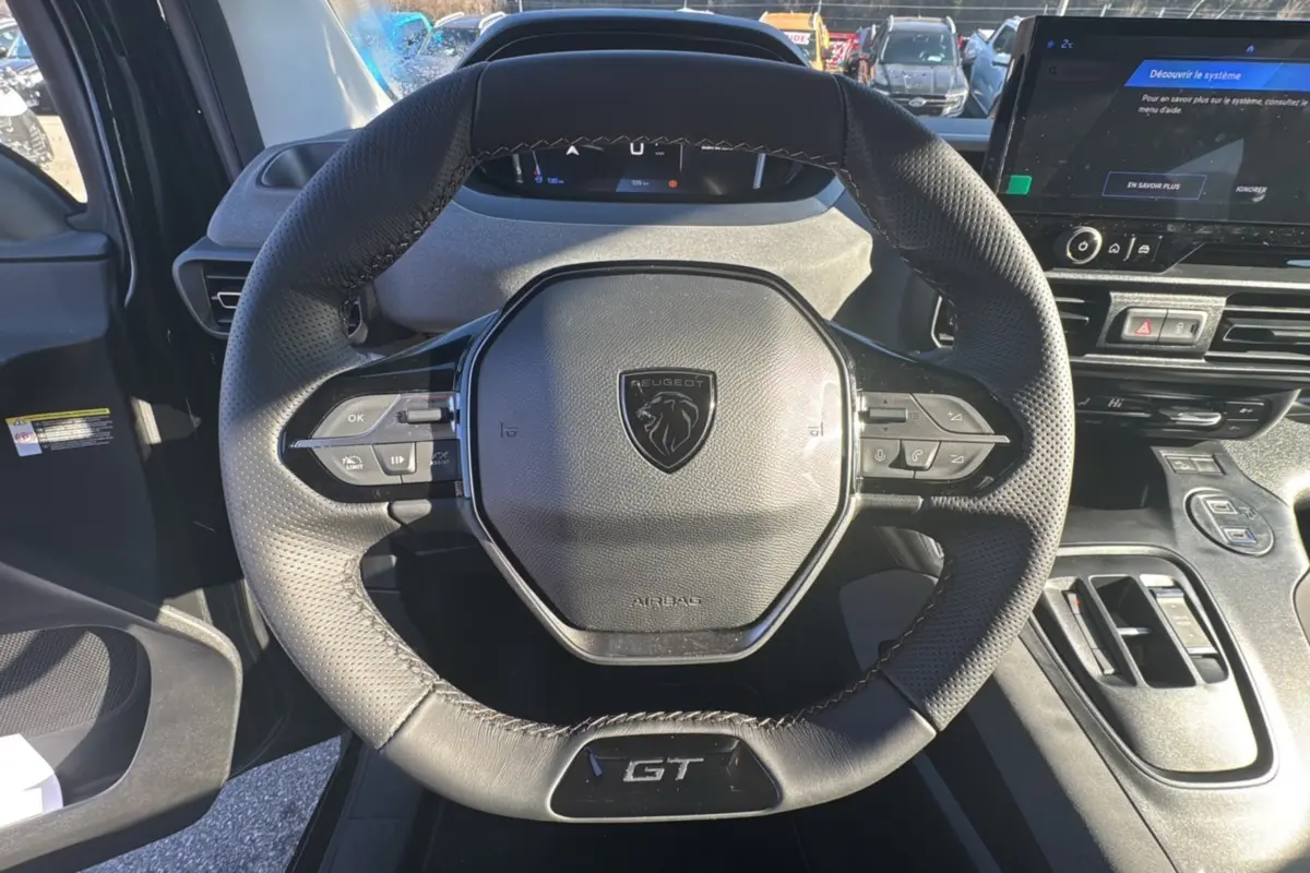 Vue rapprochée du volant cuir multifonctions noir avec logo Peugeot et badge GT du Rifter 2025, intérieur moderne.