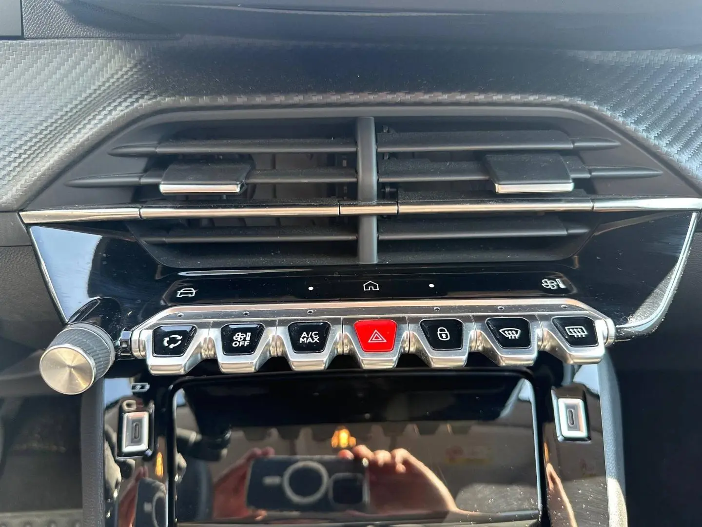 Vue rapprochée de la console centrale noire brillante de la Peugeot 208 2025 avec boutons argentés et rouge d'alerte.