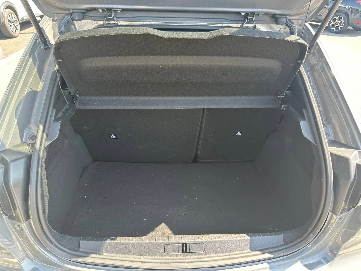 Coffre ouvert vu de l’arrière d’une Peugeot 208 1.2 100ch gris Selenium, montrant l’espace de chargement vide.