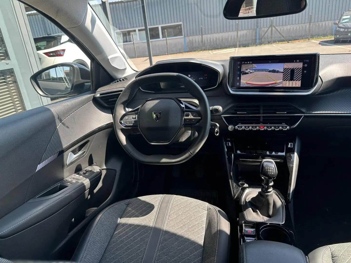 Vue intérieure avant de la Peugeot 208 1.2 100ch gris Selenium, volant compact et écran tactile avec caméra de recul visible.