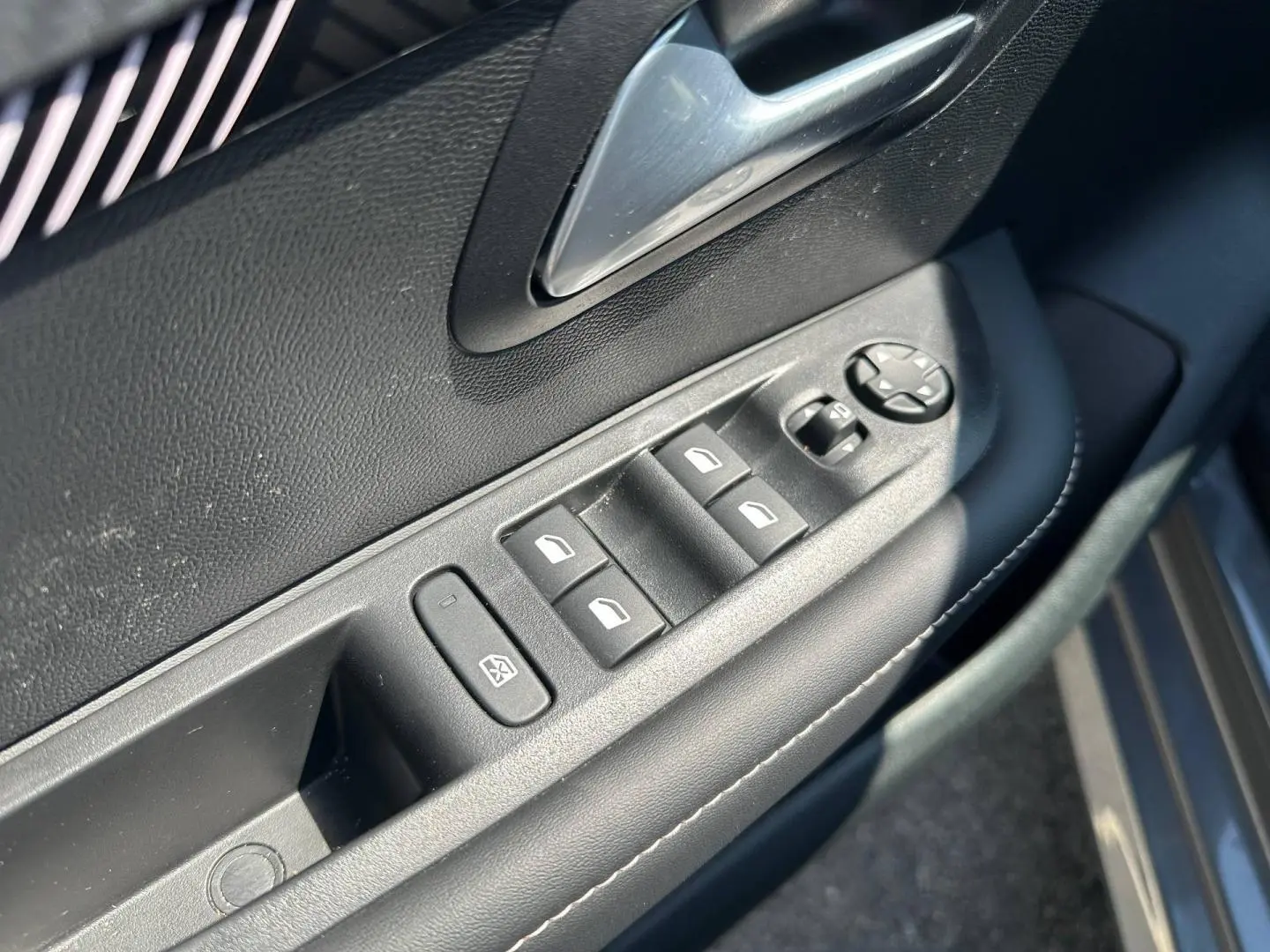 Gros plan sur la commande des vitres électriques côté gauche d’une Peugeot 208 gris Selenium avec poignée argentée.