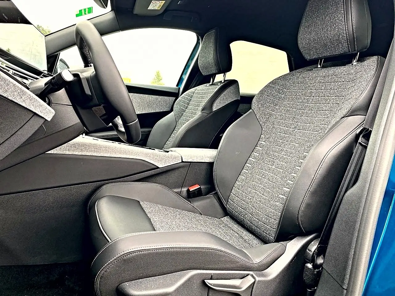 Vue intérieure côté conducteur du Peugeot 3008 bleu 2025, mettant en valeur les sièges bi-matière gris et noir et le volant cuir.