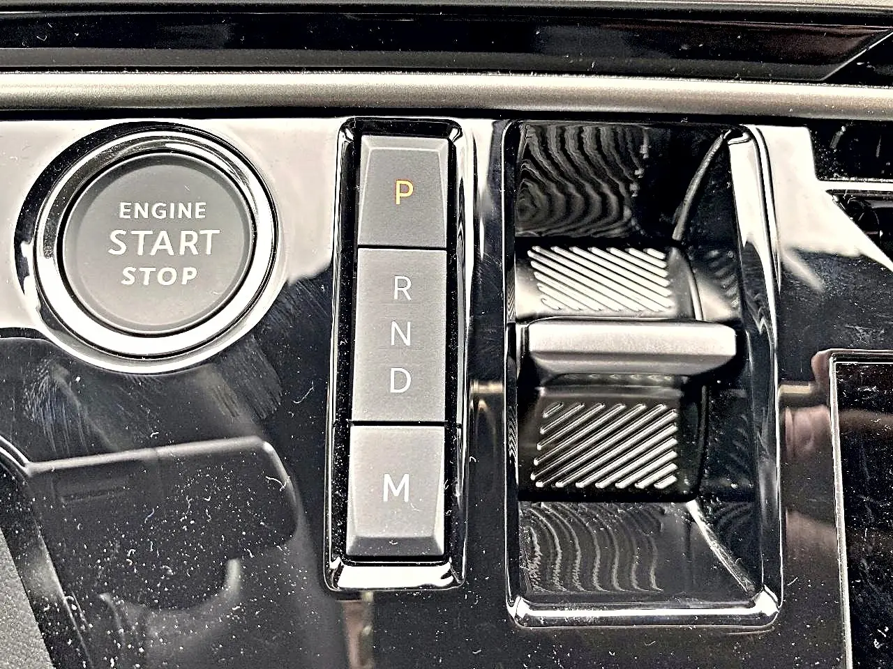 Gros plan sur la console centrale noire brillante du Peugeot 3008 1.2 hybrid 145 allure e-dcs6 avec bouton start/stop et sélecteur de boîte auto.