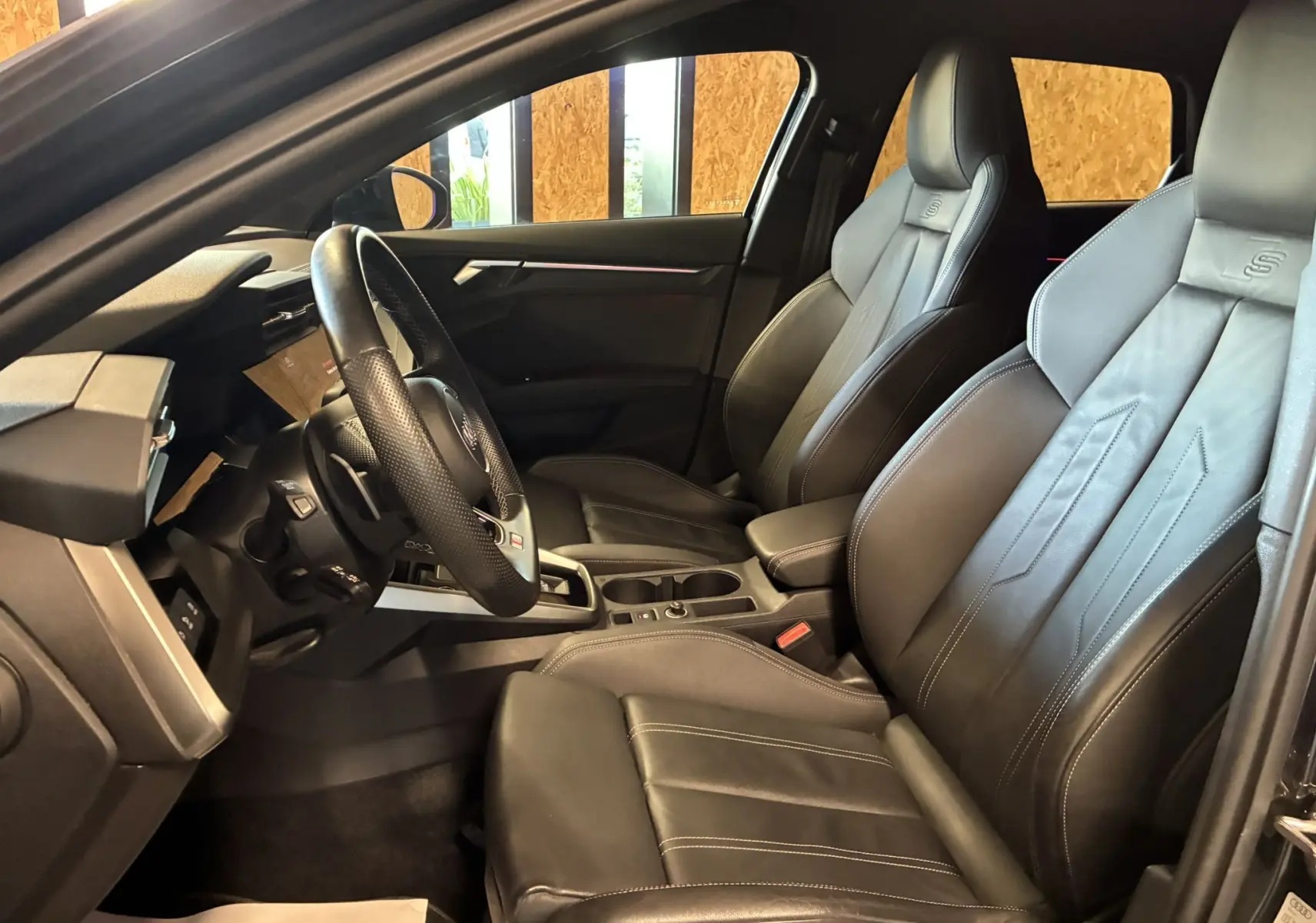 Vue intérieure côté conducteur de l'Audi A3 Sportback 2022 avec sièges cuir noirs S Line et volant multifonction.