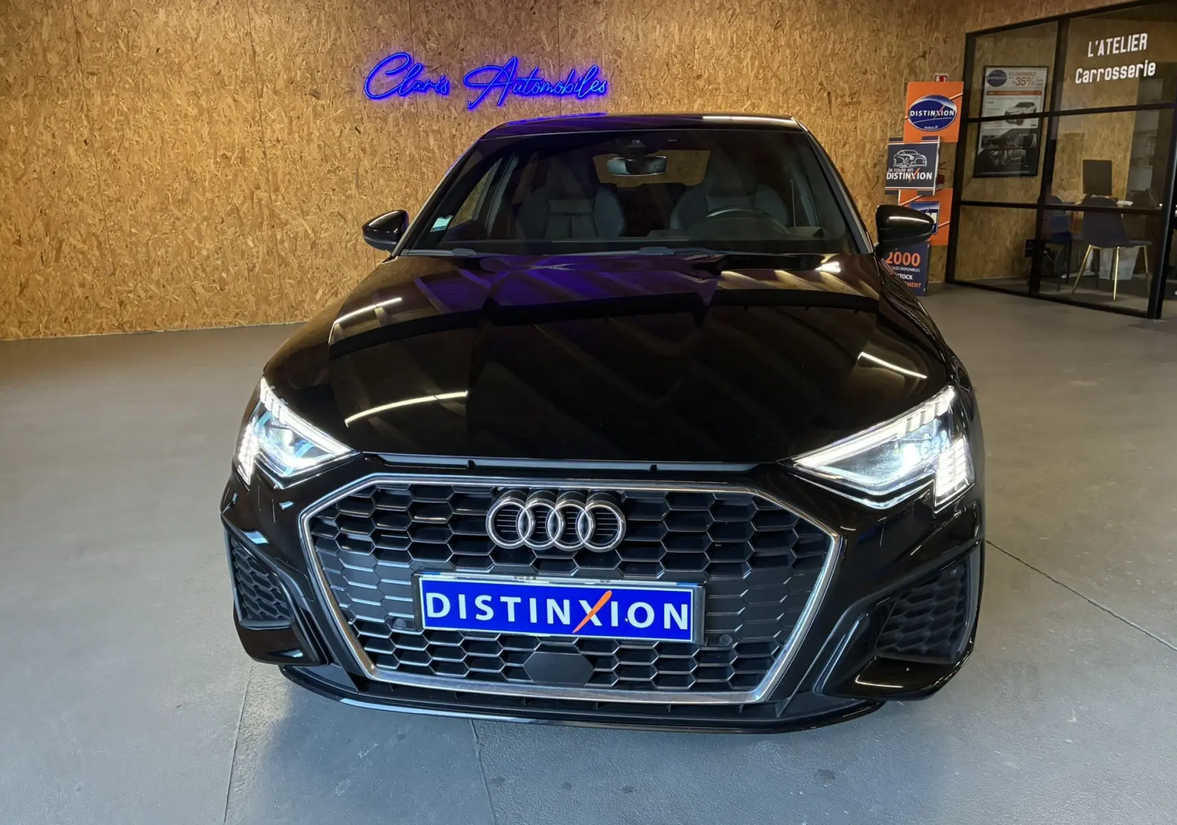 Vue frontale d'une Audi A3 Sportback noire 2022 avec calandre hexagonale et phares LED allumés en intérieur showroom.