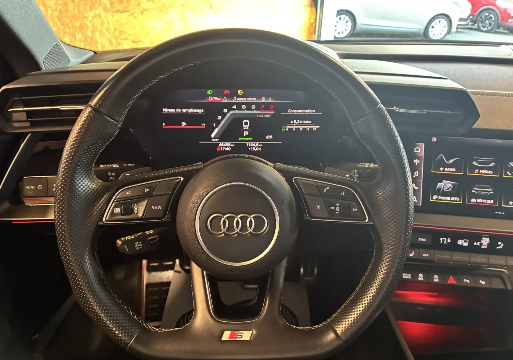 Vue rapprochée du volant en cuir noir perforé avec logo Audi et S Line, tableau de bord digital et écran central lumineux.