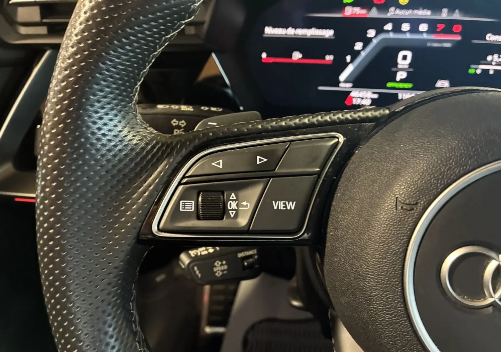 Gros plan sur le volant en cuir noir de l'Audi A3 Sportback 2022, avec commandes multifonctions et tableau de bord numérique en arrière-plan.