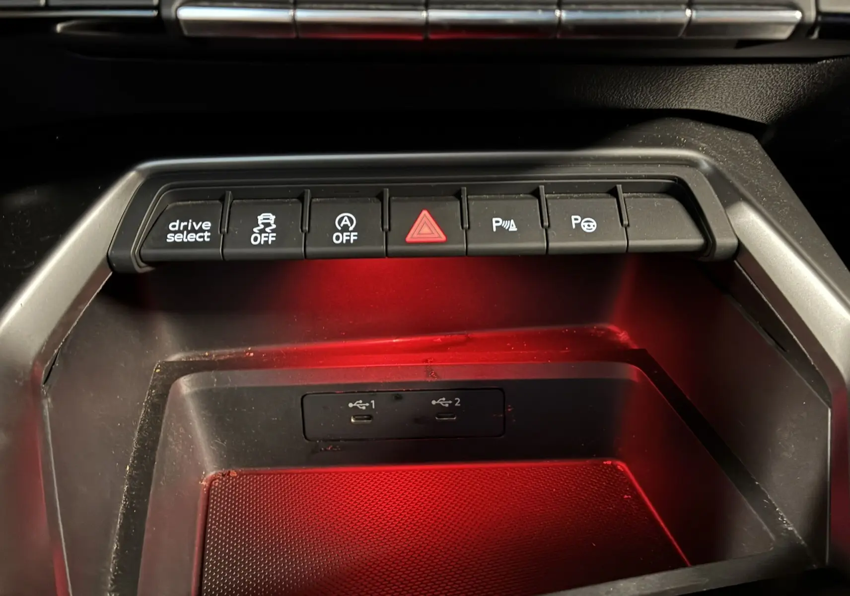 Gros plan sur la console centrale noire de l'Audi A3 Sportback 2022, avec boutons de contrôle et éclairage rouge intérieur.