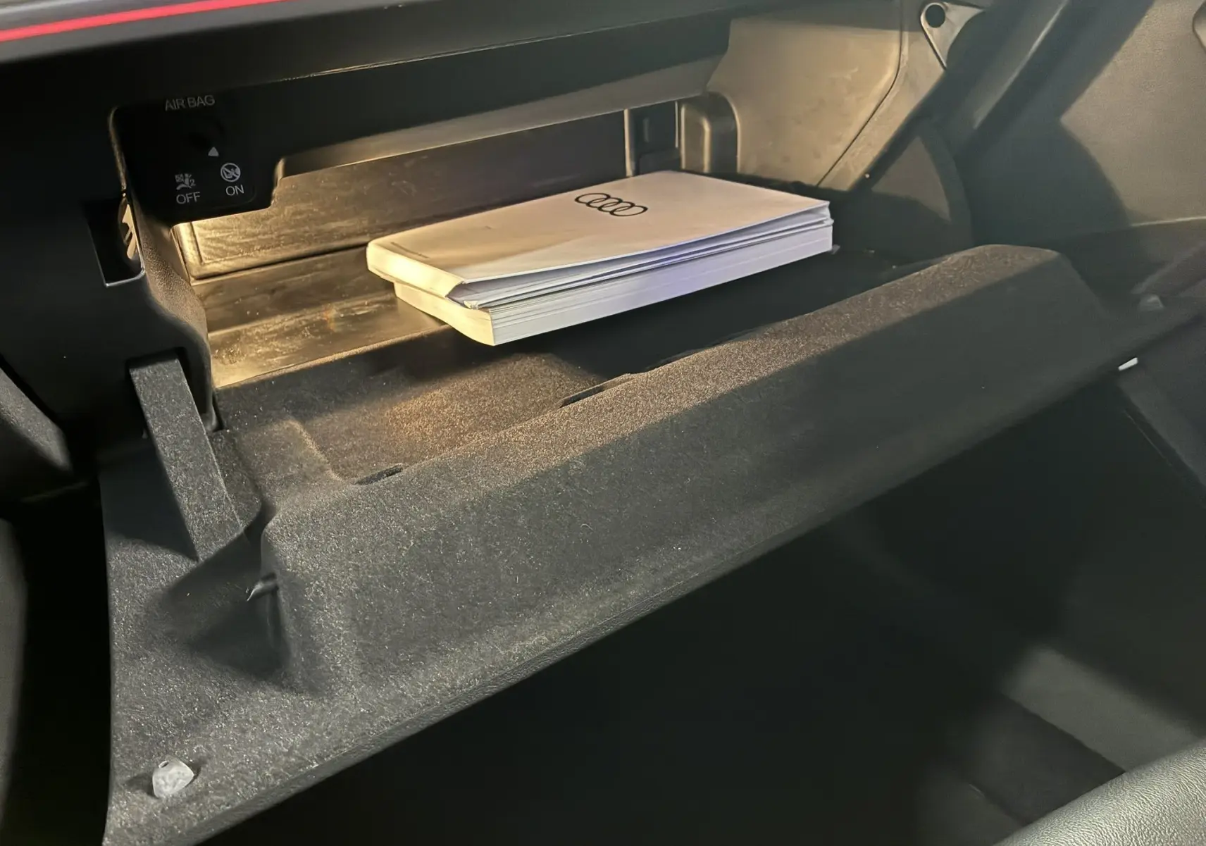 Gros plan sur la boîte à gants ouverte de l'Audi A3 Sportback noire 2022, avec manuel Audi visible à l'intérieur.