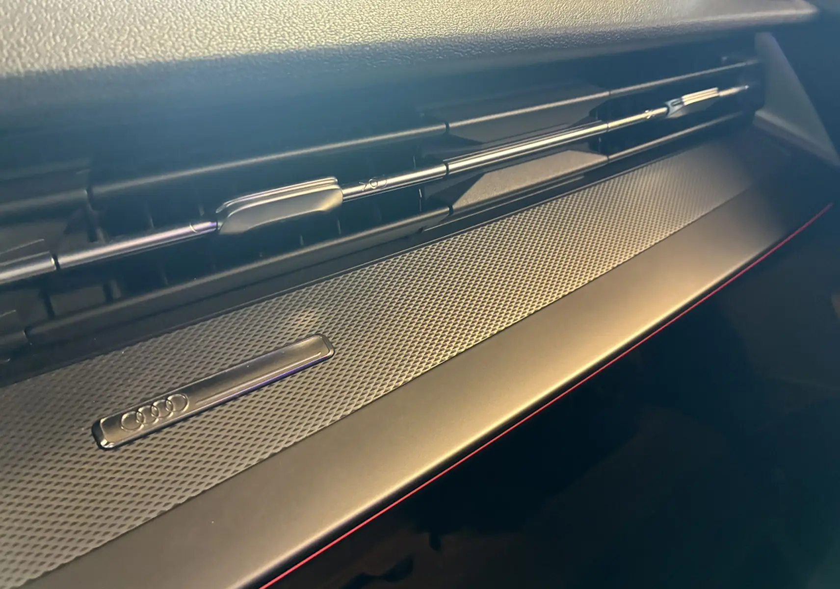 Détail du tableau de bord noir de l'Audi A3 Sportback 2022 avec bandeau décoratif texturé et logo Audi chromé.