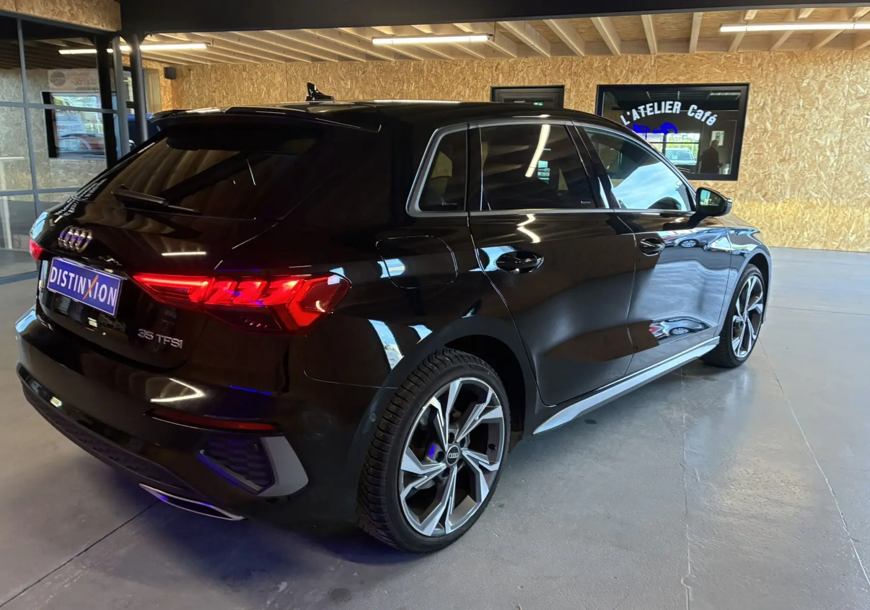 Audi A3 Sportback noir vue 3/4 arrière droit en intérieur, feux arrière allumés et jantes alliage distinctives.