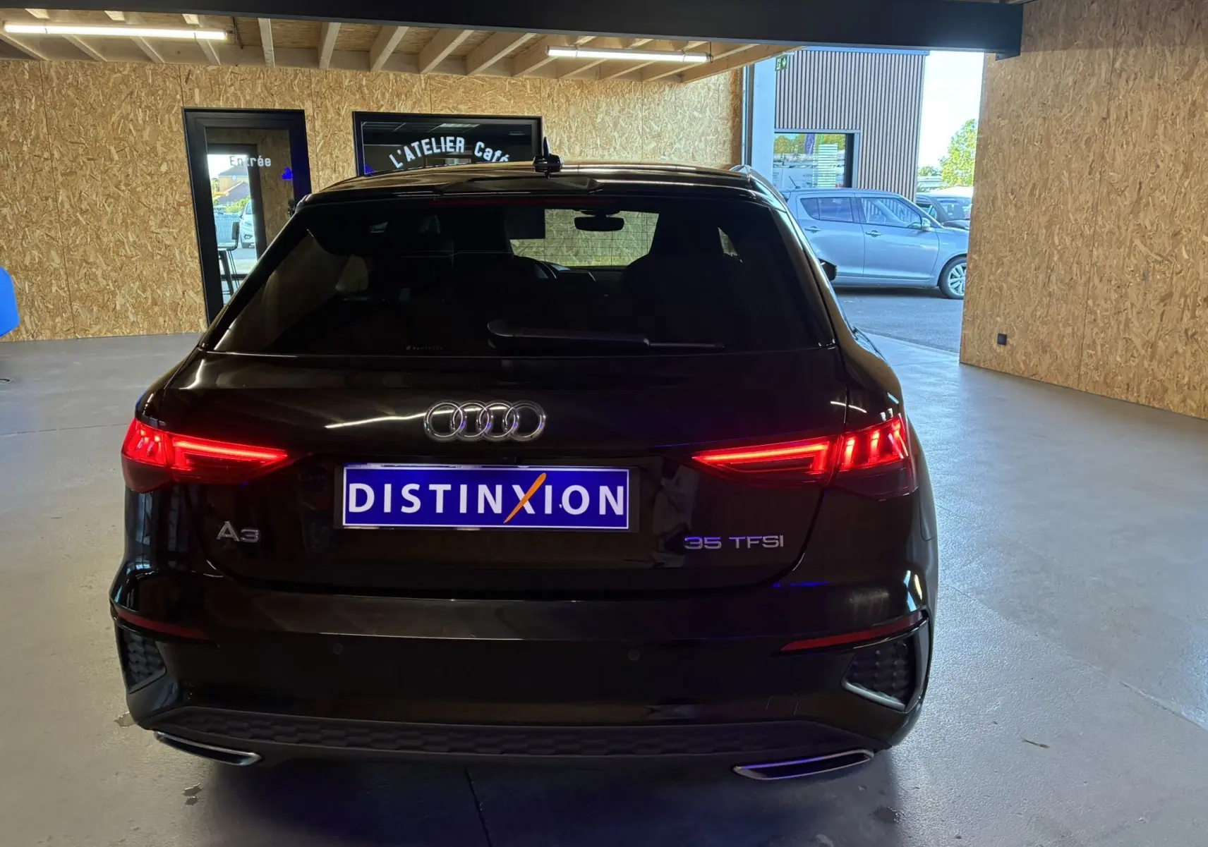 Vue arrière d'une Audi A3 Sportback noire 35 TFSI avec feux allumés dans un garage lumineux.