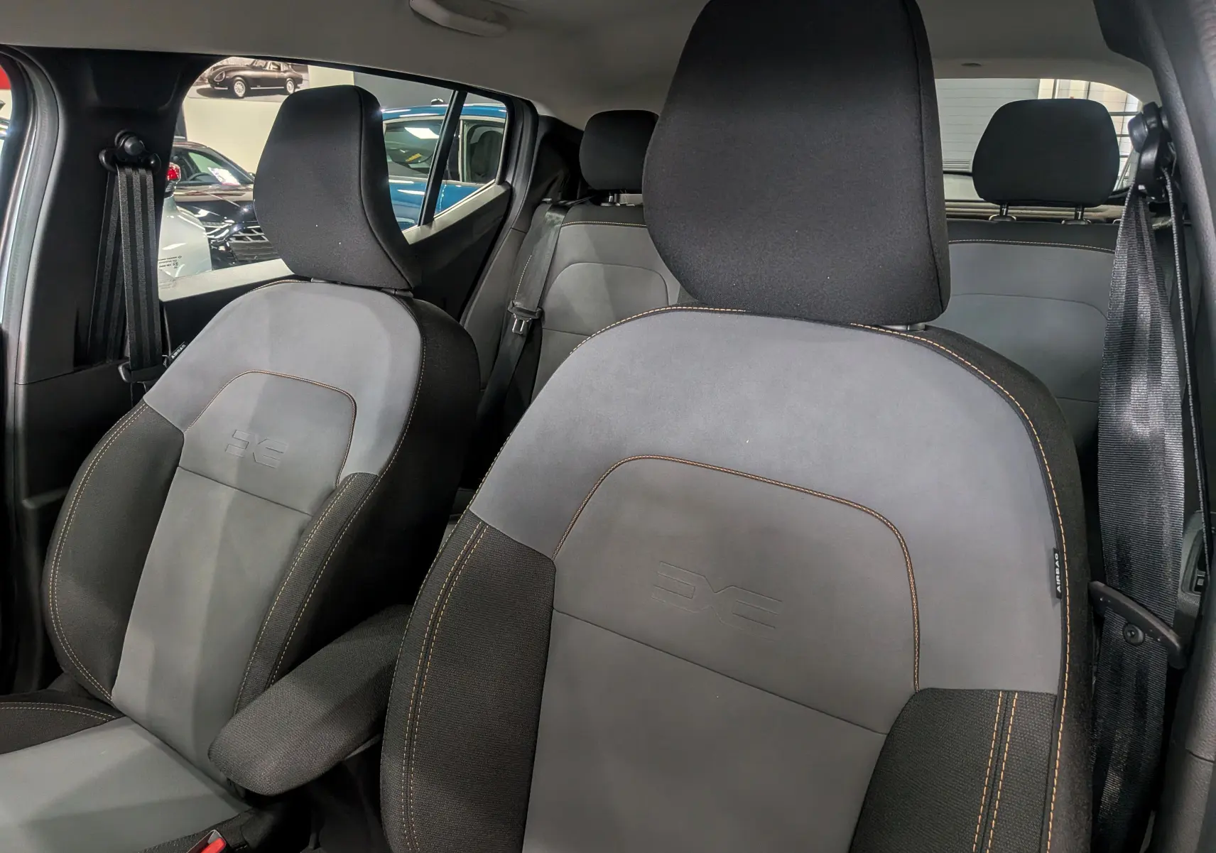 Vue intérieure rapprochée des sièges avant en tissu gris et noir avec surpiqûres orange du Dacia Sandero Stepway 2025.