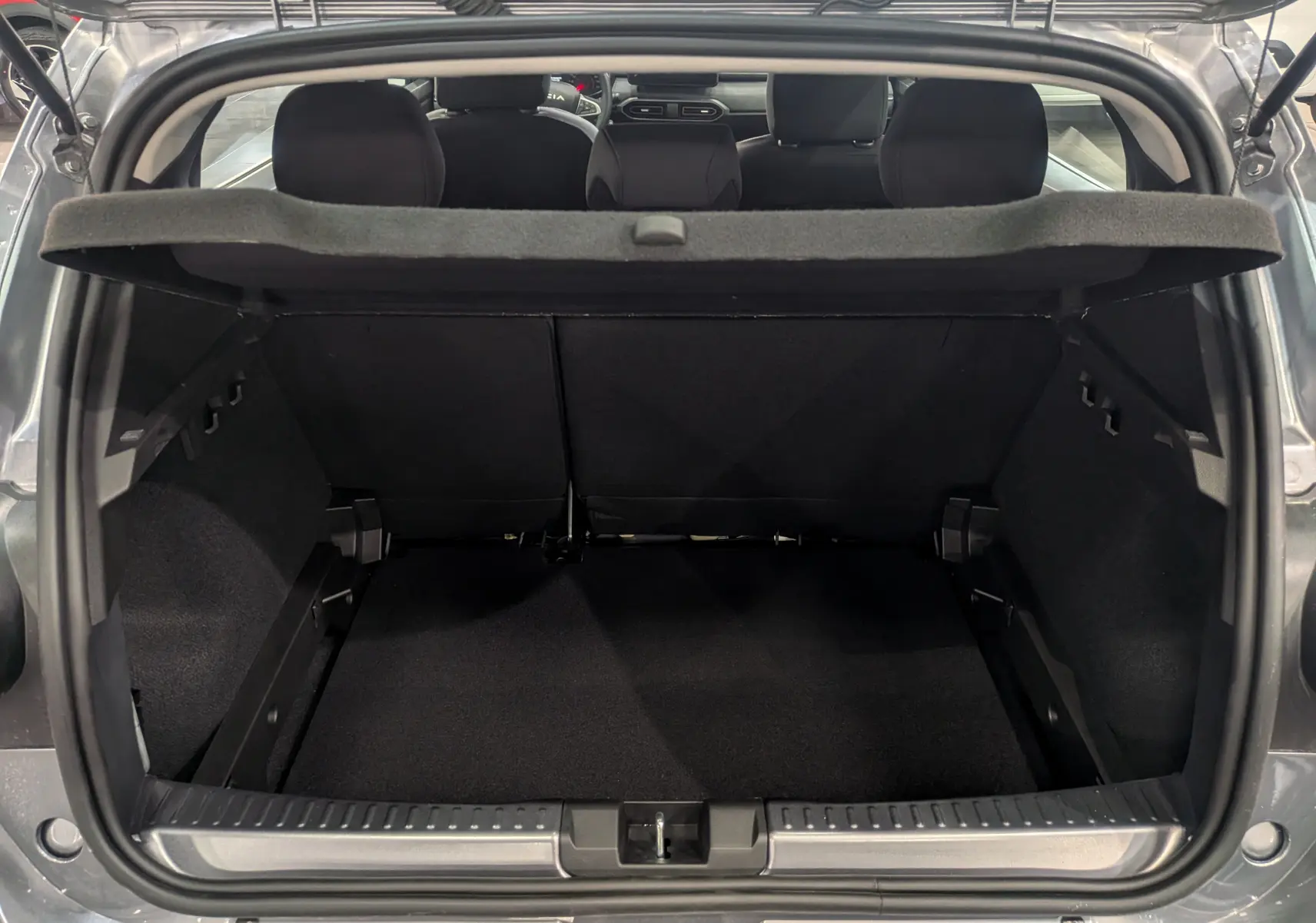 Coffre ouvert vu de l'arrière d'une Dacia Sandero Stepway TCe 110 Gris Schiste avec banquette arrière et cache-bagages visibles.