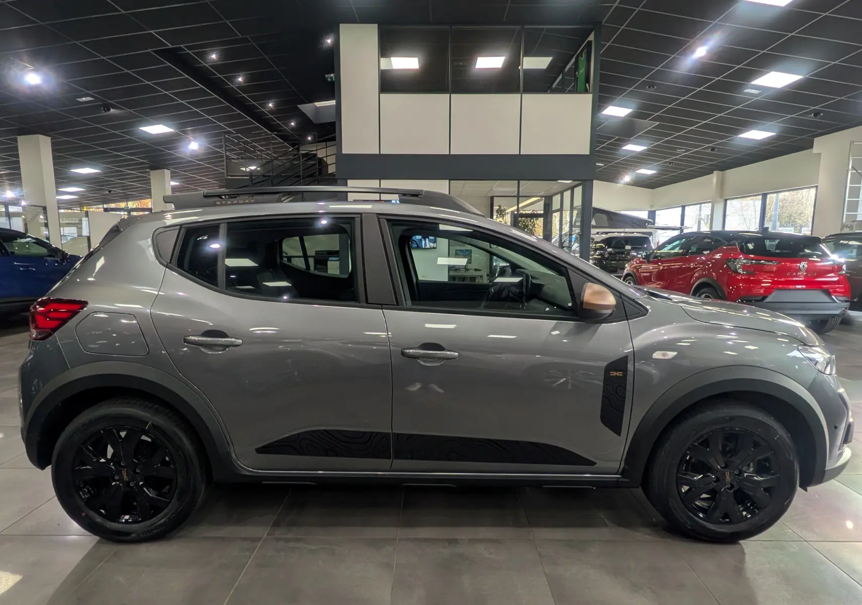 Profil droit d'une Dacia Sandero Stepway TCe 110 Gris Schiste avec jantes noires et stickers noirs distinctifs sur les portières.
