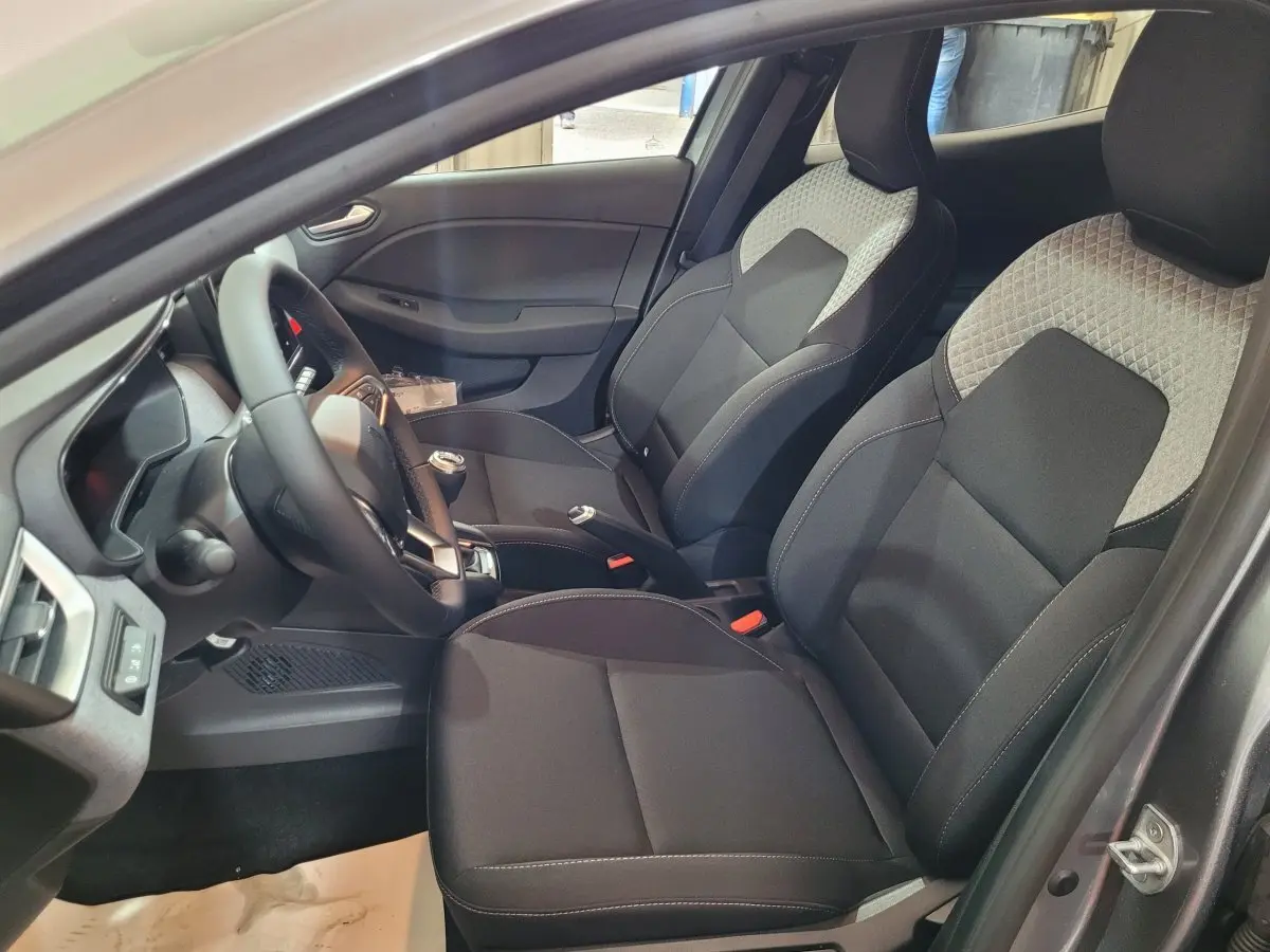 Intérieur avant droit de la Renault Clio gris foncé 2025, sièges bi-ton noirs et gris avec volant multifonctions.