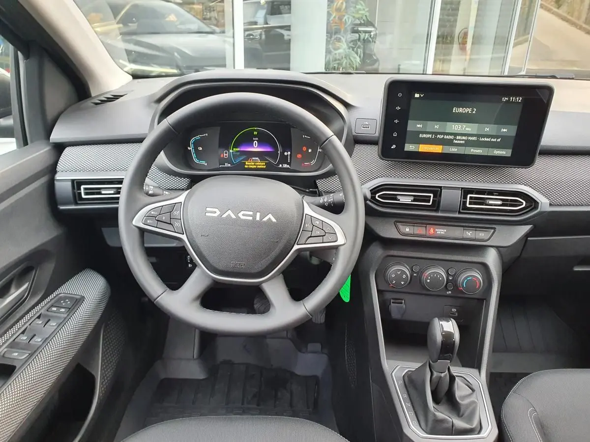 Vue intérieure frontale du tableau de bord du Dacia Jogger 2024, avec volant multifonction, écran tactile et levier de boîte auto.