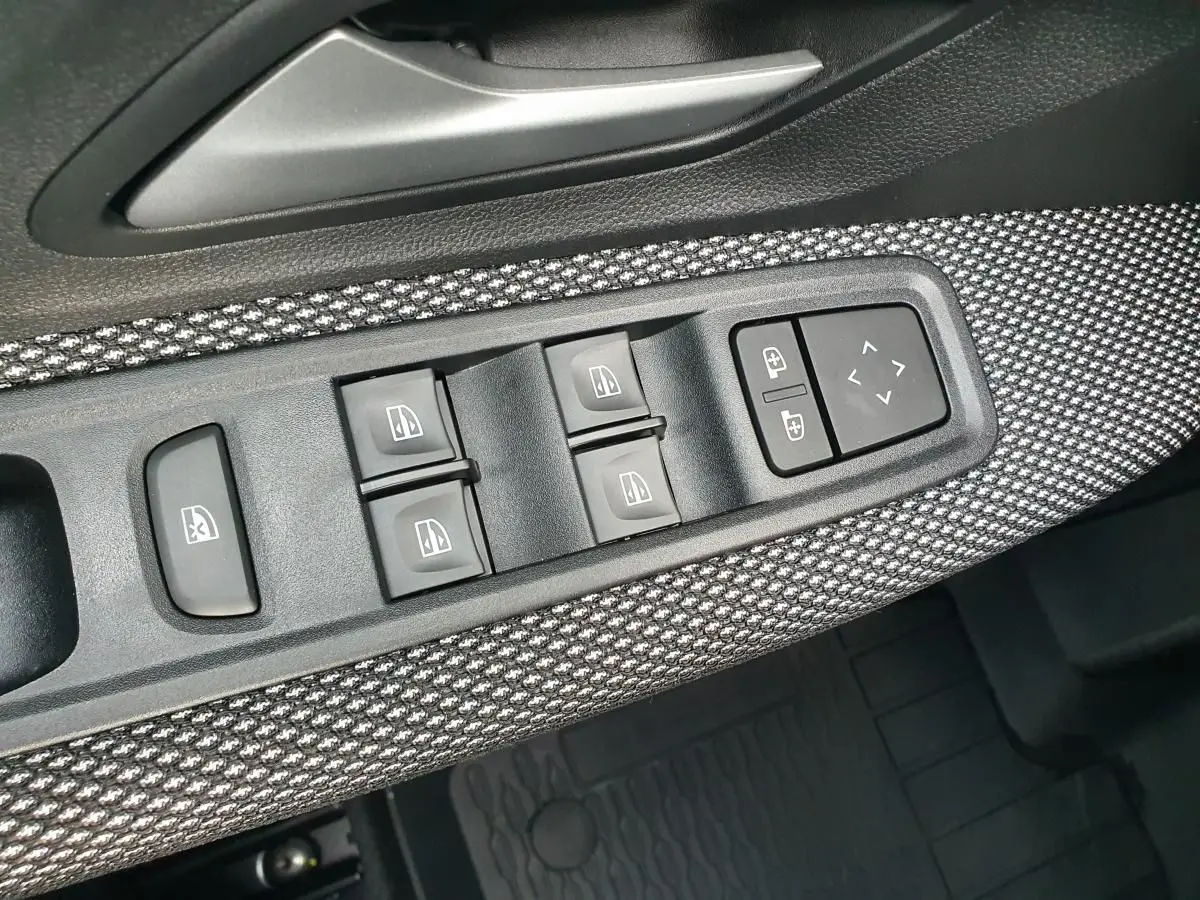 Gros plan sur la commande des vitres et rétroviseurs côté conducteur avec habillage tissu gris et noir.