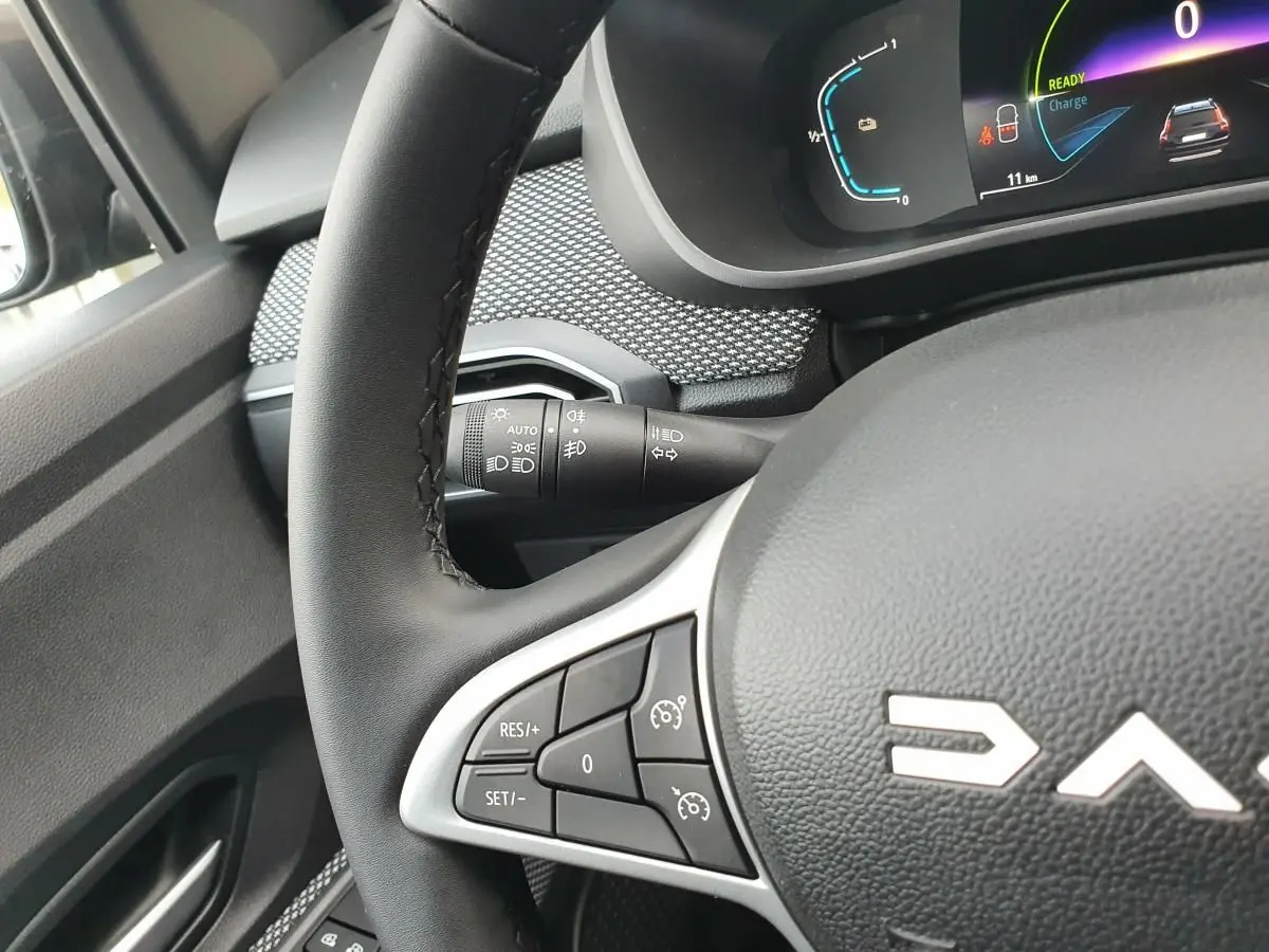 Gros plan sur le volant noir de la Dacia Jogger 2024 avec commandes intégrées et tableau de bord numérique partiellement visible.