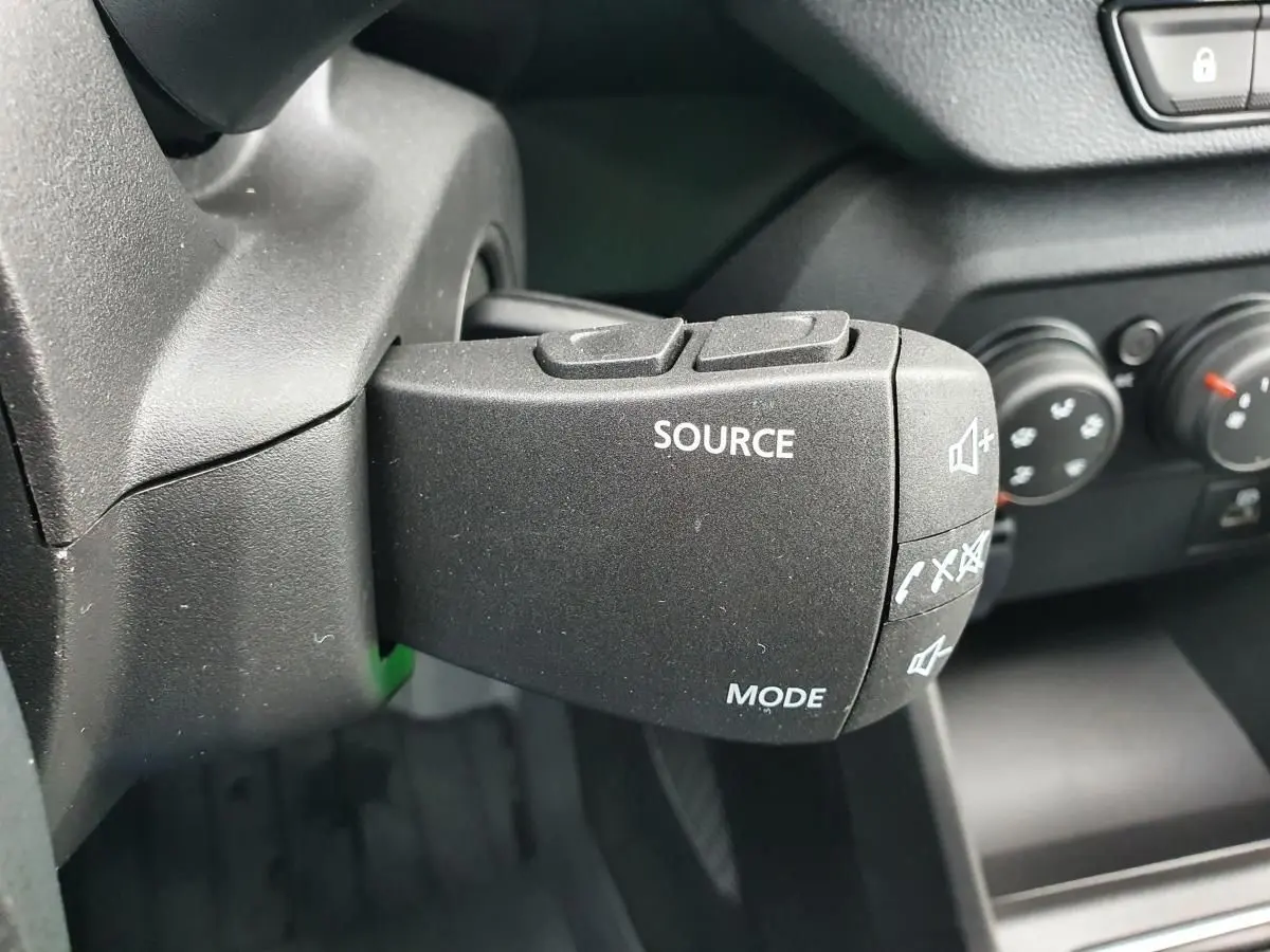 Gros plan sur la commande audio au volant du Dacia Jogger 2024, intérieur noir avec boutons source et mode visibles.
