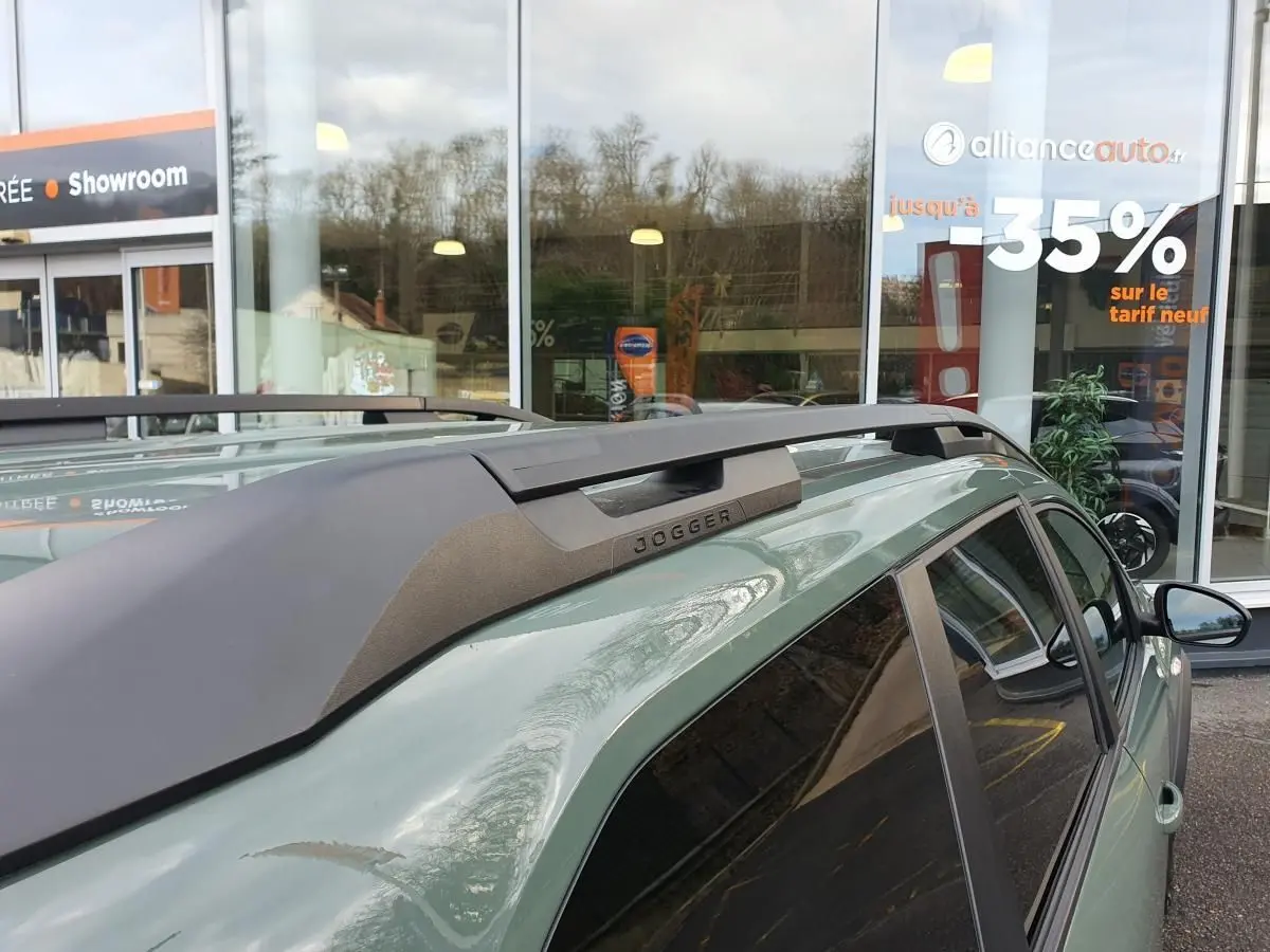 Vue rapprochée du toit côté droit du Dacia Jogger kaki métallisé avec barres de toit longitudinales et logo Jogger visible.