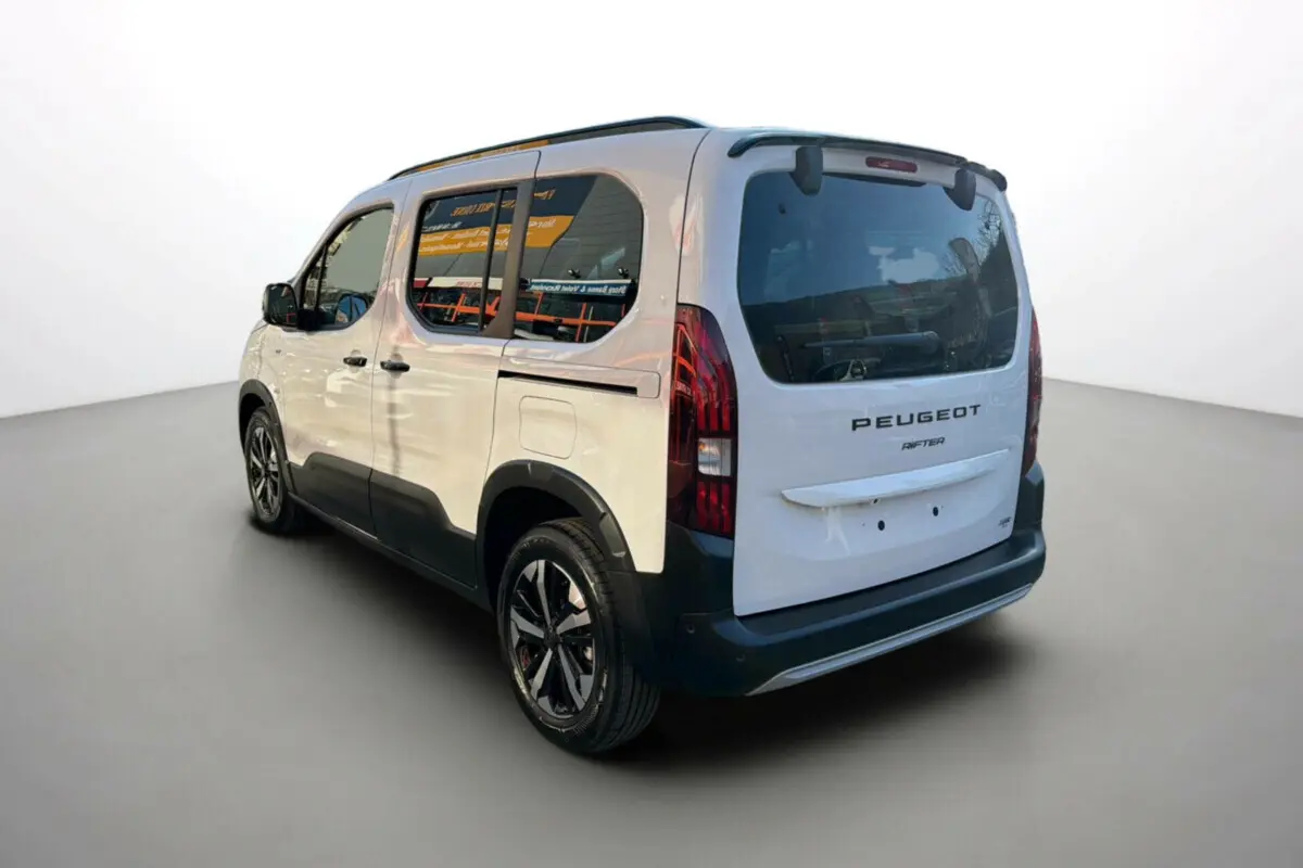 Vue 3/4 arrière droite du Peugeot Rifter blanc kaolin avec barres de toit et jantes alu noires.
