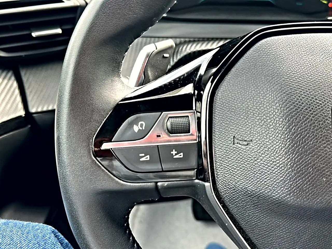 Gros plan sur le volant noir multifonction du Peugeot 2008 1.2 hybrid 145 style, avec commandes audio intégrées.
