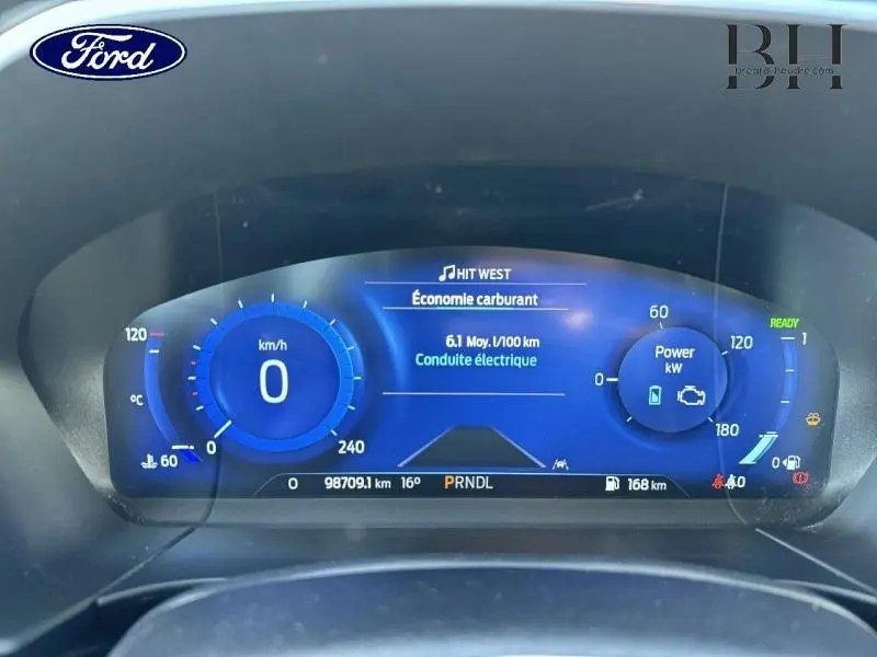 Tableau de bord numérique du Ford Kuga 2023 affichant la consommation et la puissance en mode hybride, vue frontale rapprochée.