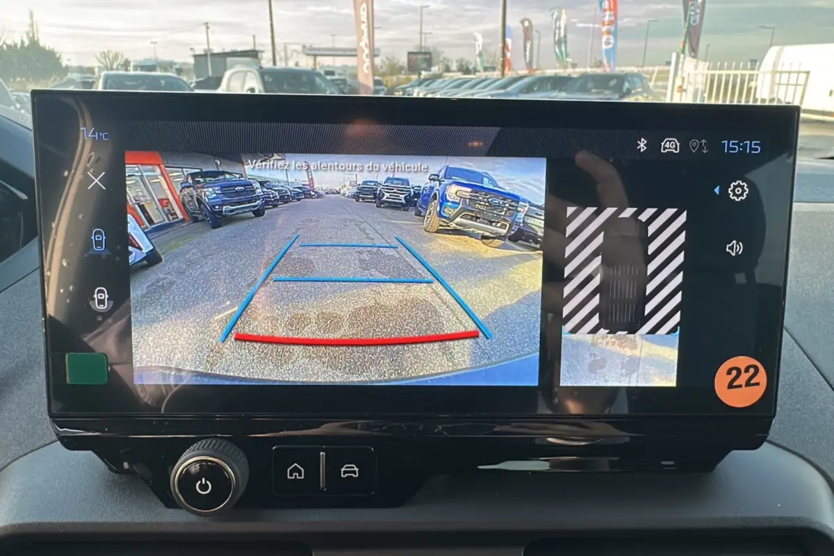 Écran tactile intérieur montrant la caméra de recul avec vue arrière sur un parking ensoleillé.