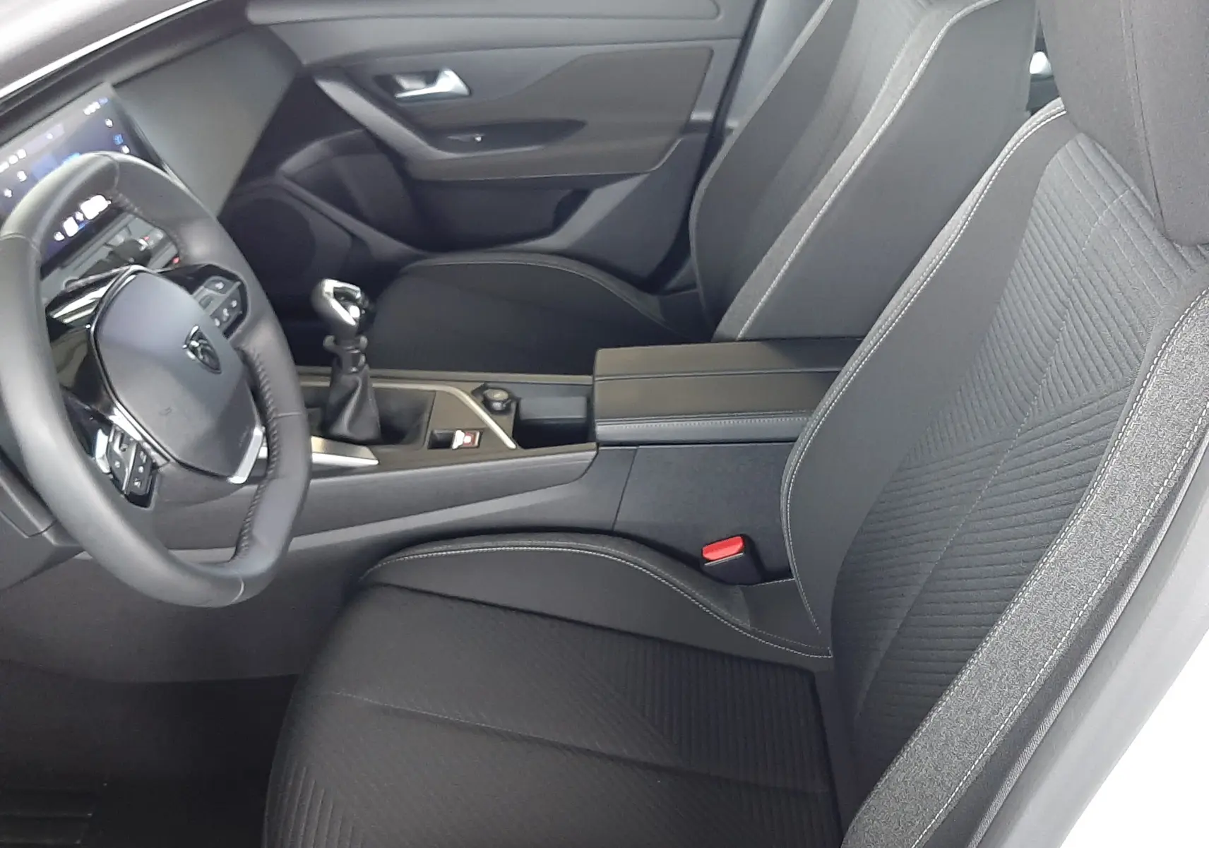 Vue intérieure côté conducteur de la Peugeot 308 2022 avec sièges tissu noir et volant multifonction.