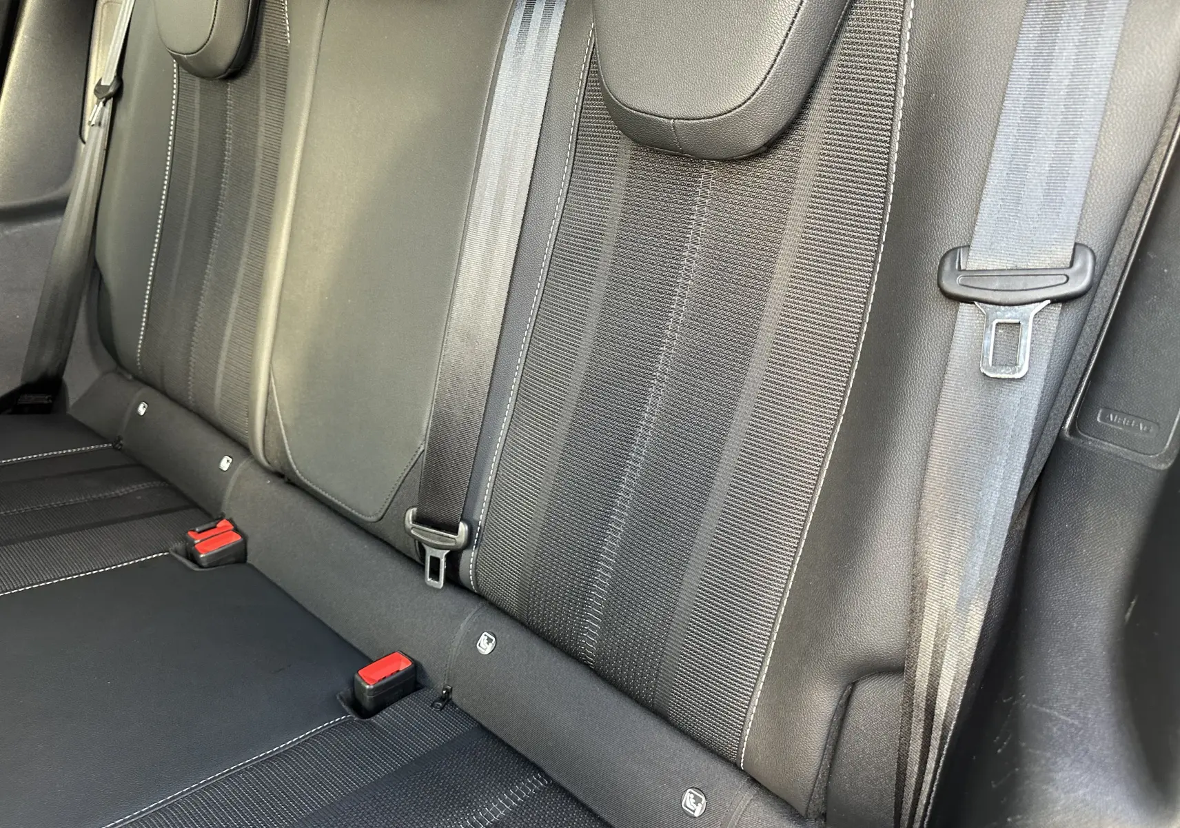 Vue rapprochée des sièges arrière noirs en tissu et cuir du Opel Mokka Elegance 2021 avec ceintures de sécurité visibles.