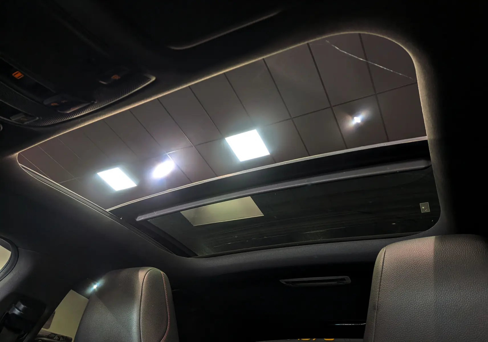 Toit ouvrant panoramique vu de l'intérieur sur les sièges en cuir noir d'une Mercedes Classe CLA 200 Fascination 2017.