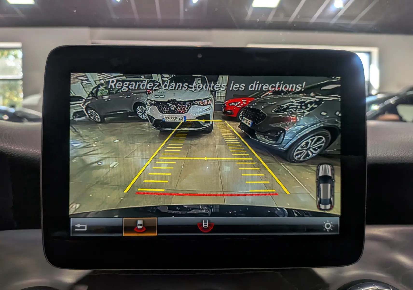 Vue de la caméra de recul sur l'écran du Mercedes CLA 200 Fascination bleu Cavansite, avec lignes de guidage jaunes et rouges.