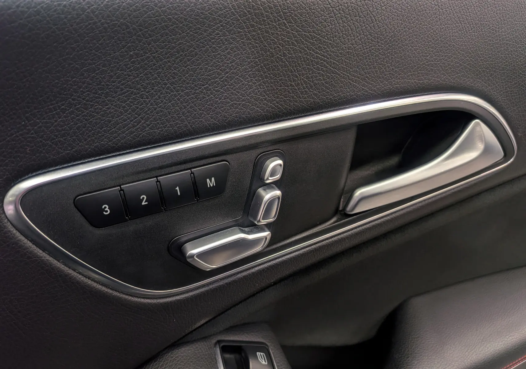 Gros plan sur la commande de réglage électrique des sièges côté gauche en cuir noir de la Mercedes CLA 200 Fascination.