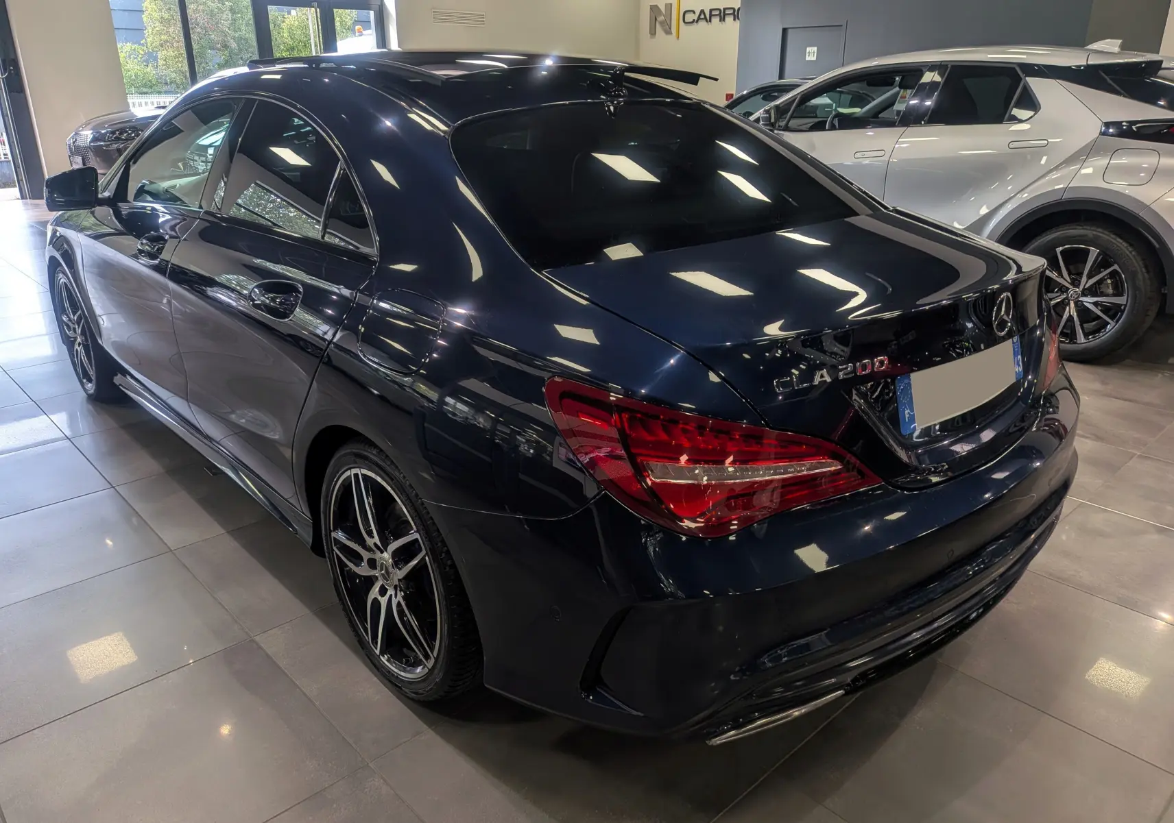 Vue 3/4 arrière droite d'une Mercedes Classe CLA 200 Fascination bleu Cavansite avec jantes AMG bicolores en showroom.