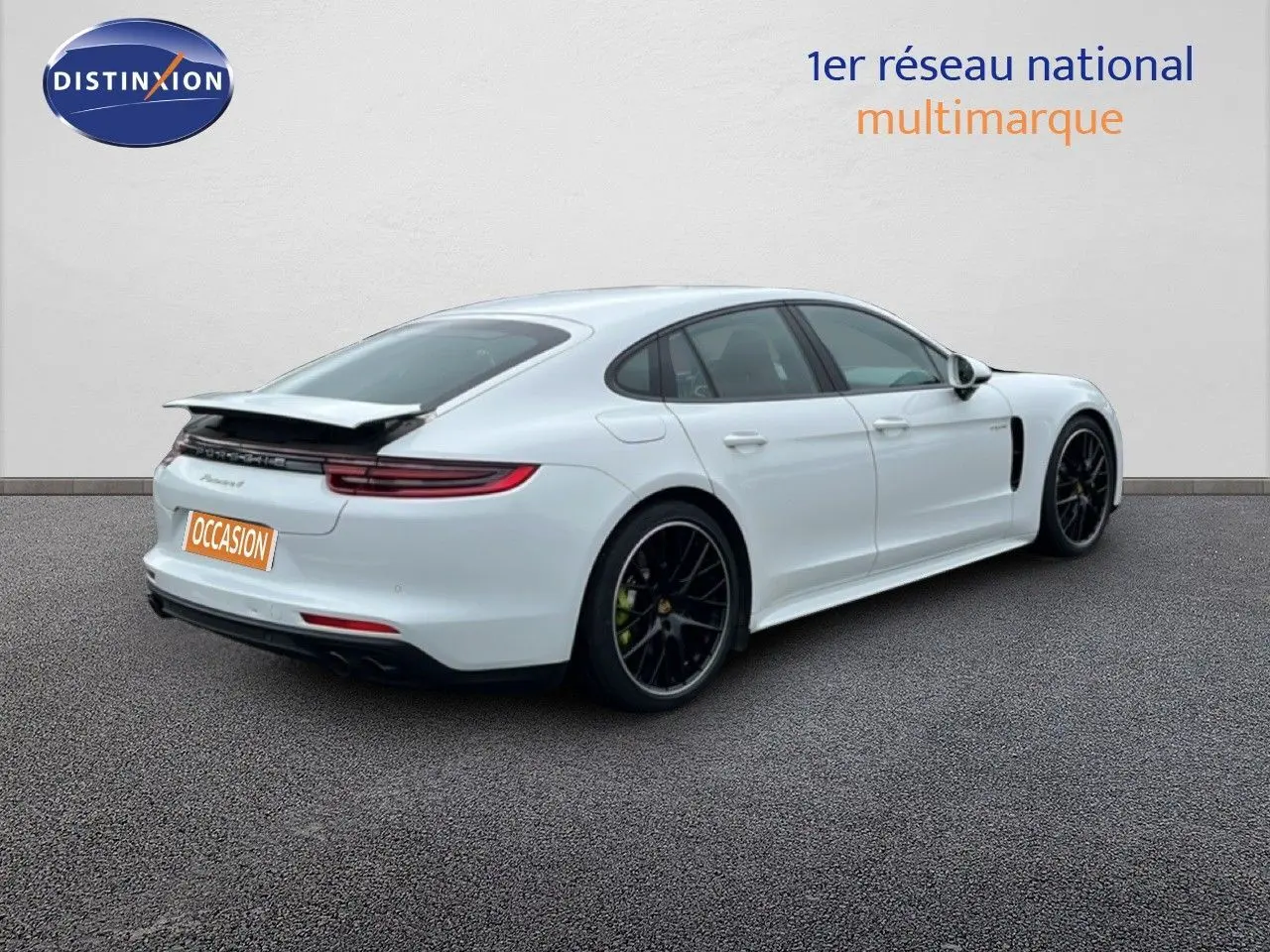 Vue 3/4 arrière droite d'une Porsche Panamera 4 E-Hybrid blanche avec jantes noires sport et aileron relevé.