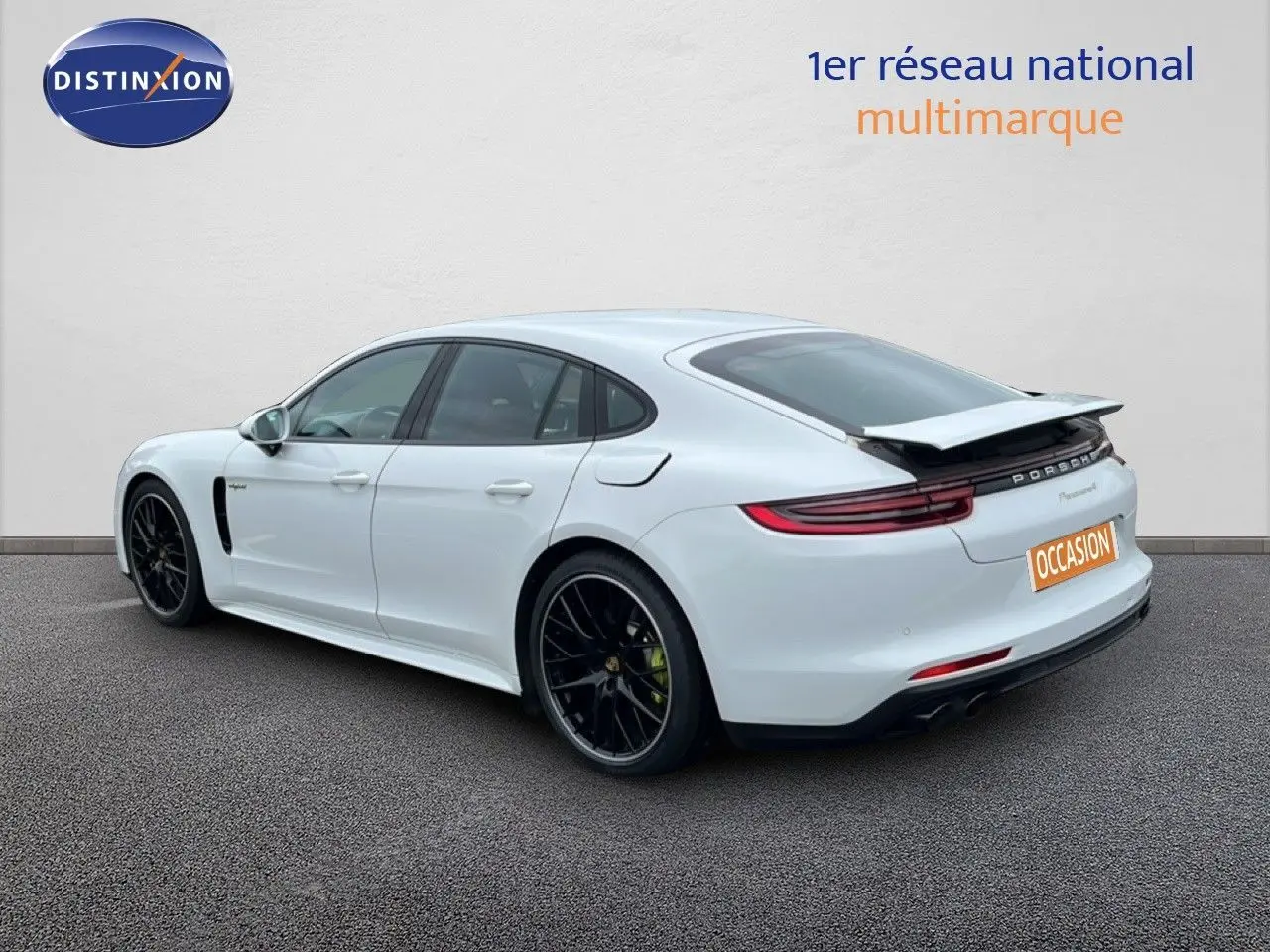 Vue 3/4 arrière droite d'une Porsche Panamera 4 E-Hybrid blanche avec jantes sport noires et aileron déployé.