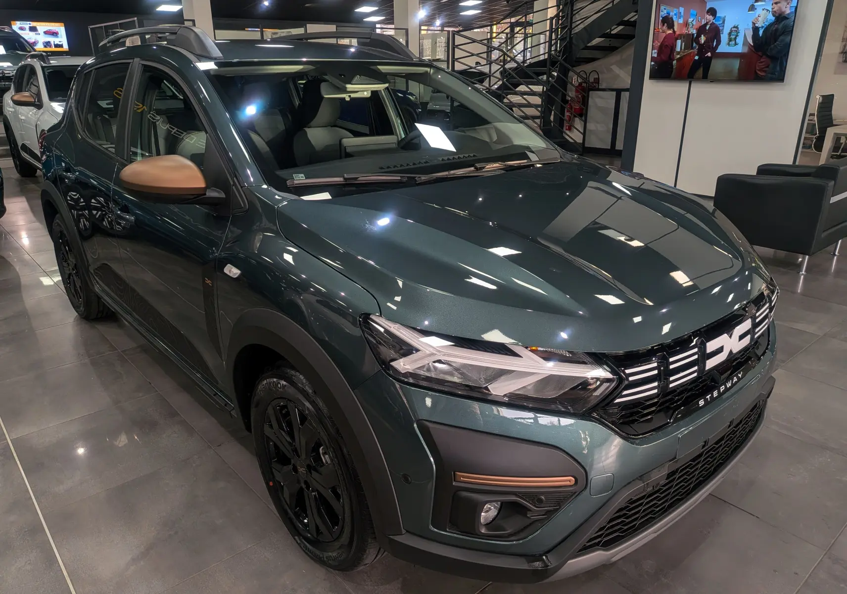 Dacia Sandero Stepway TCe 110 vert cèdre en 3/4 avant droit, avec rétroviseurs bronze et jantes noires en showroom.