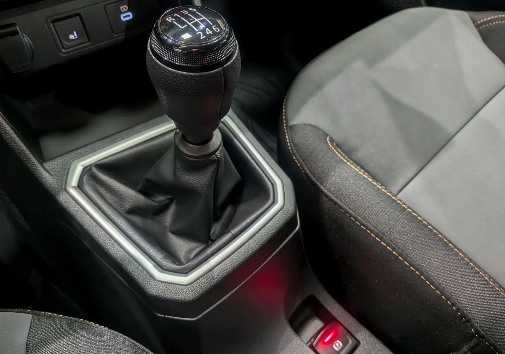 Gros plan sur le levier de vitesse manuel noir et la sellerie tissu gris avec surpiqûres orange du Dacia Sandero Stepway 2025.