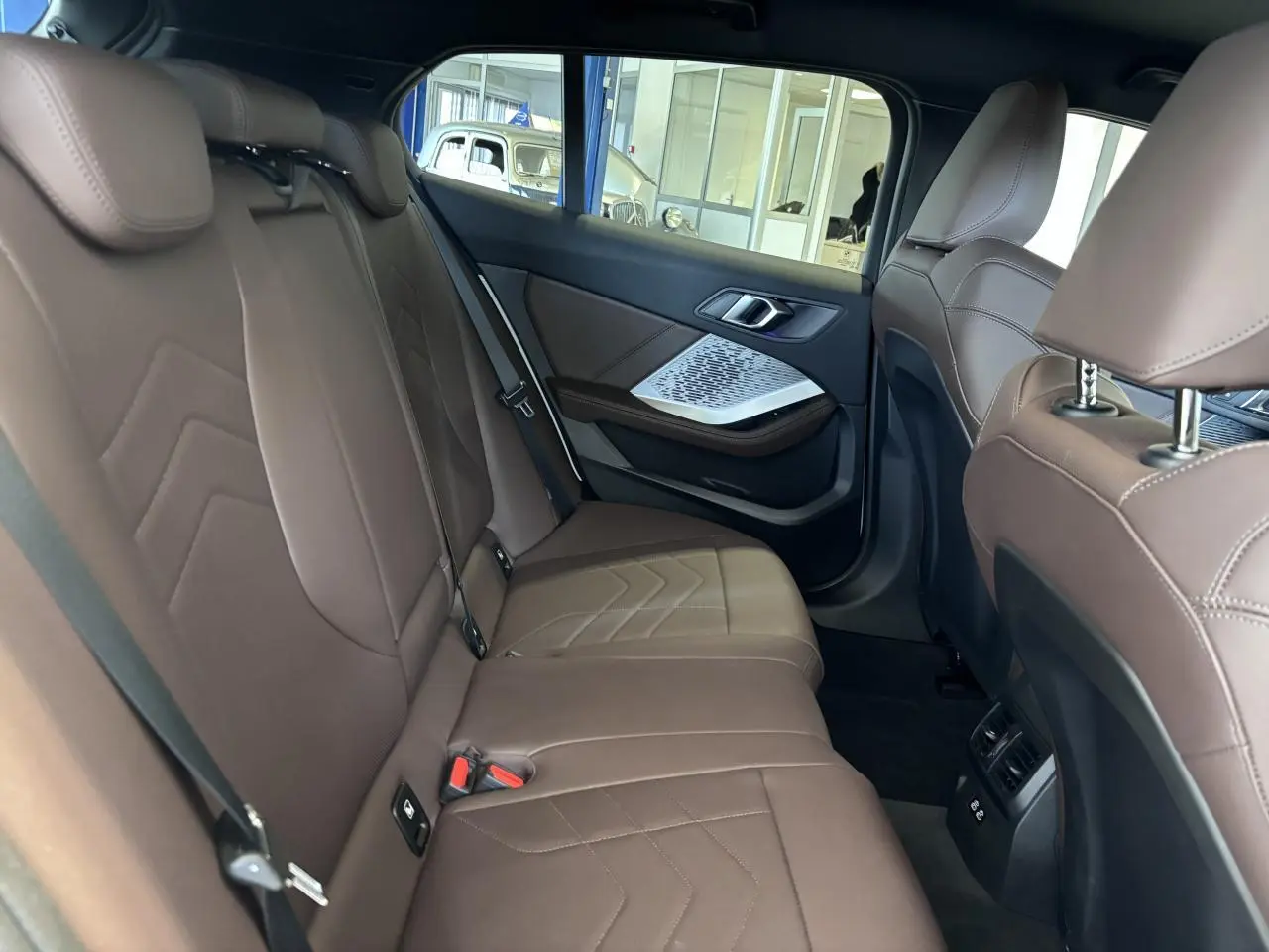 Vue intérieure arrière de la BMW Série 1 120d M Sport 2025, sièges en cuir marron et détails argentés sur les portes.