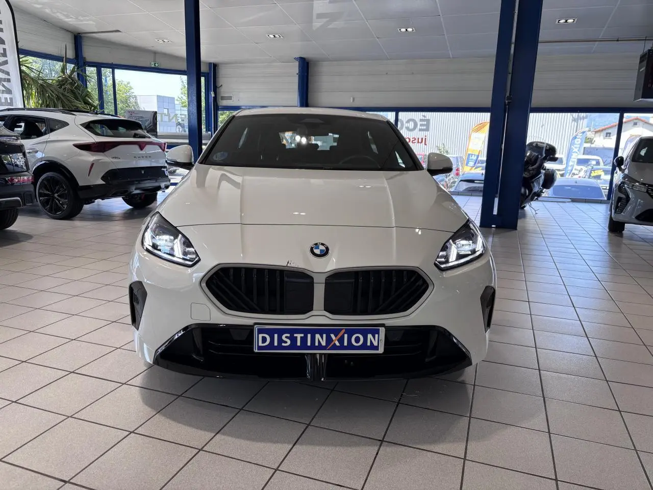 Vue avant d'une BMW Série 1 120d blanche 2025 en finition M Sport, avec calandre noire et phares allumés.
