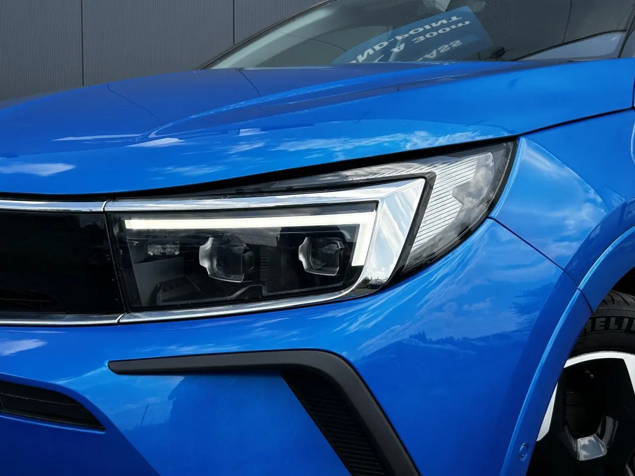 Gros plan sur le phare avant droit et la calandre d’un Opel Grandland bleu Vertigo avec jante alliage noire.