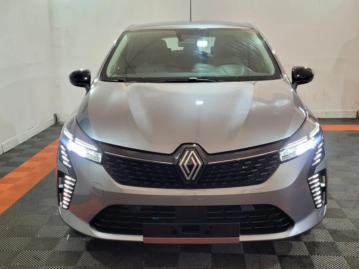 Renault Clio gris foncé vue de face, phares LED allumés et calandre noire distinctive en intérieur.