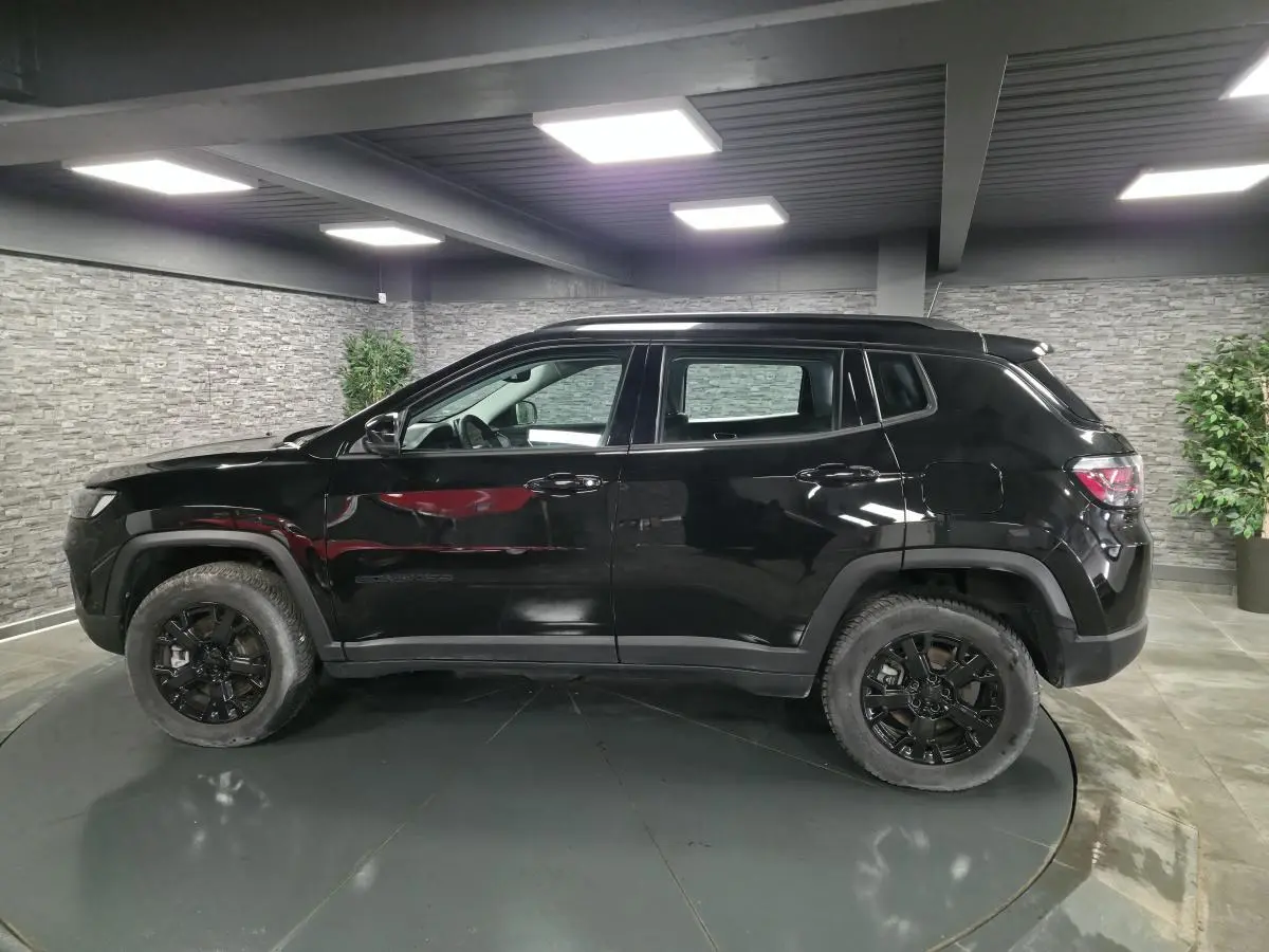 Profil côté gauche du Jeep Compass noir 2024 avec jantes noires et garde au sol surélevée en intérieur showroom.