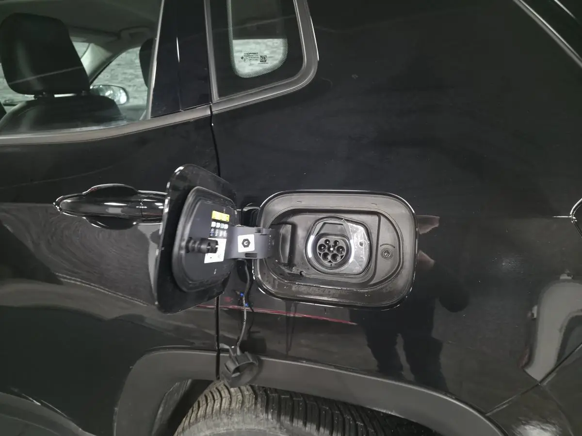Prise de recharge ouverte côté arrière gauche d'un Jeep Compass noir hybride rechargeable 2024, détail de la trappe et connecteur.