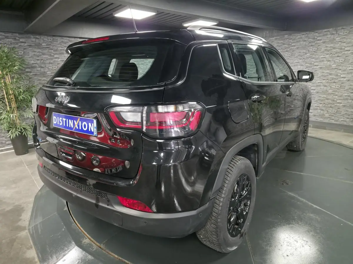 Vue 3/4 arrière droite d'un Jeep Compass noir avec jantes noires et feux arrière LED dans un showroom.