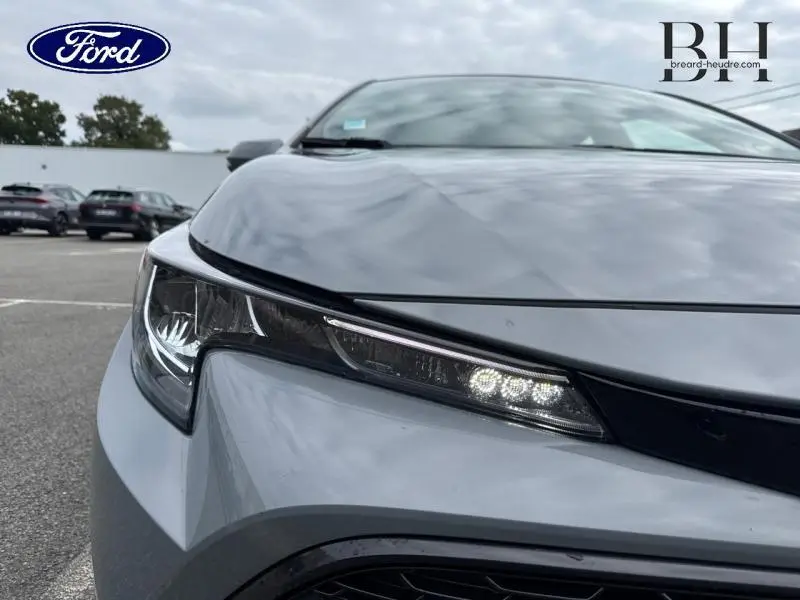 Gros plan sur le phare avant gauche d'une Toyota Corolla gris Manhattan métallisé, mettant en valeur les feux LED fins.