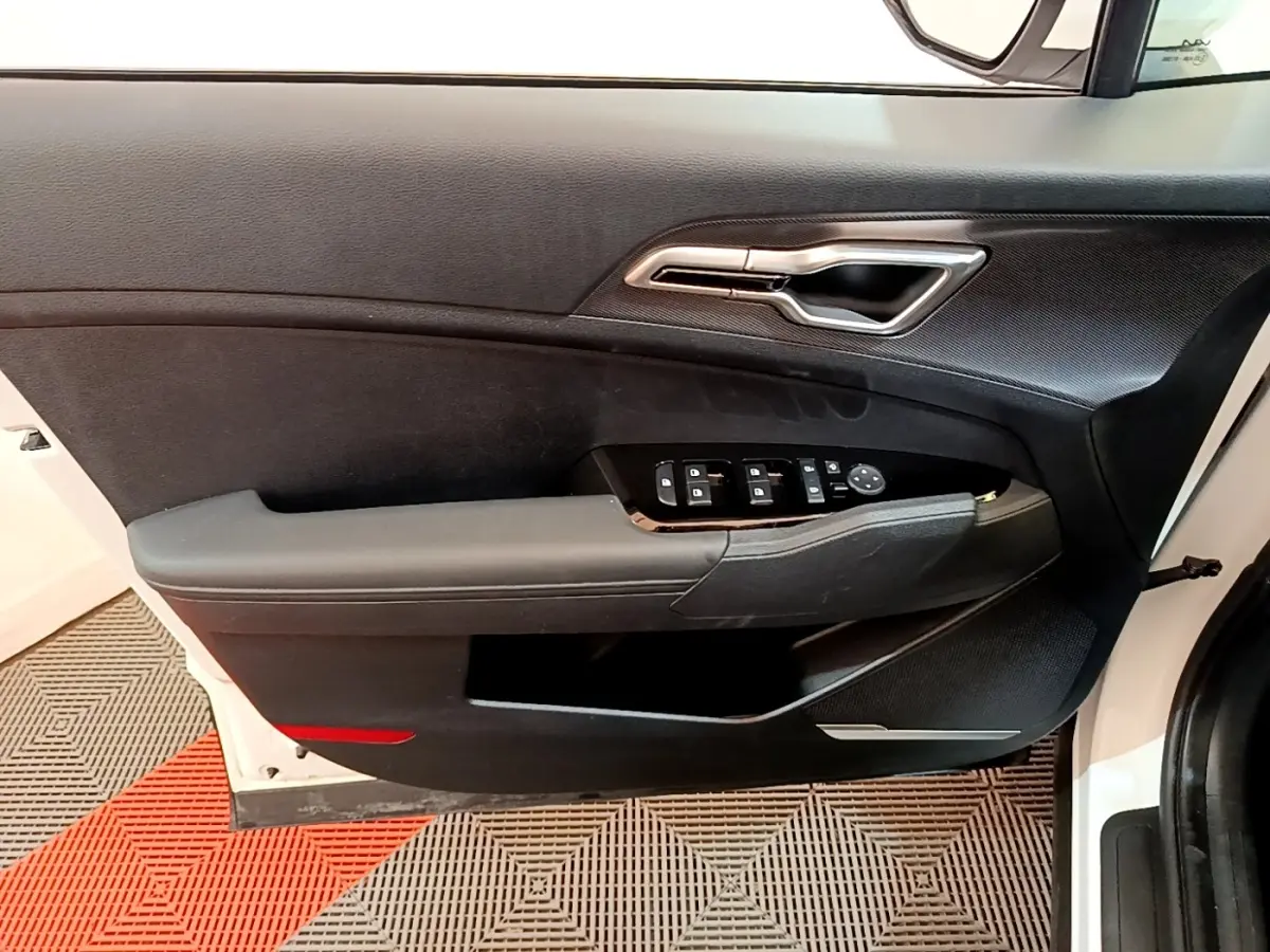 Vue intérieure de la porte avant gauche blanche du KIA SPORTAGE 2022 avec commandes électriques et poignée chromée.